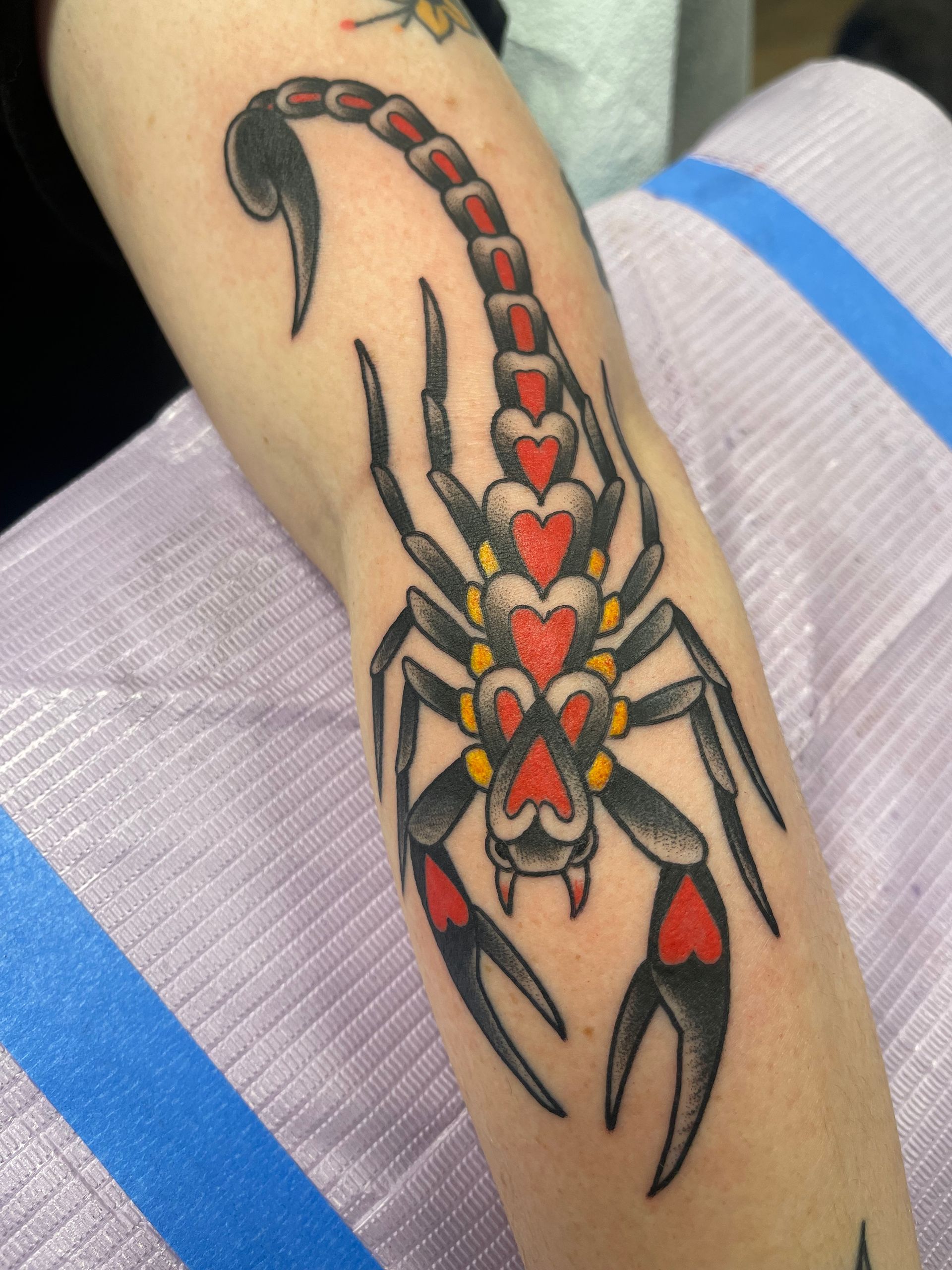 Tattoo of a scorpion on an arm. Scorpion's body is red hearts, black legs and tail, and yellow details.