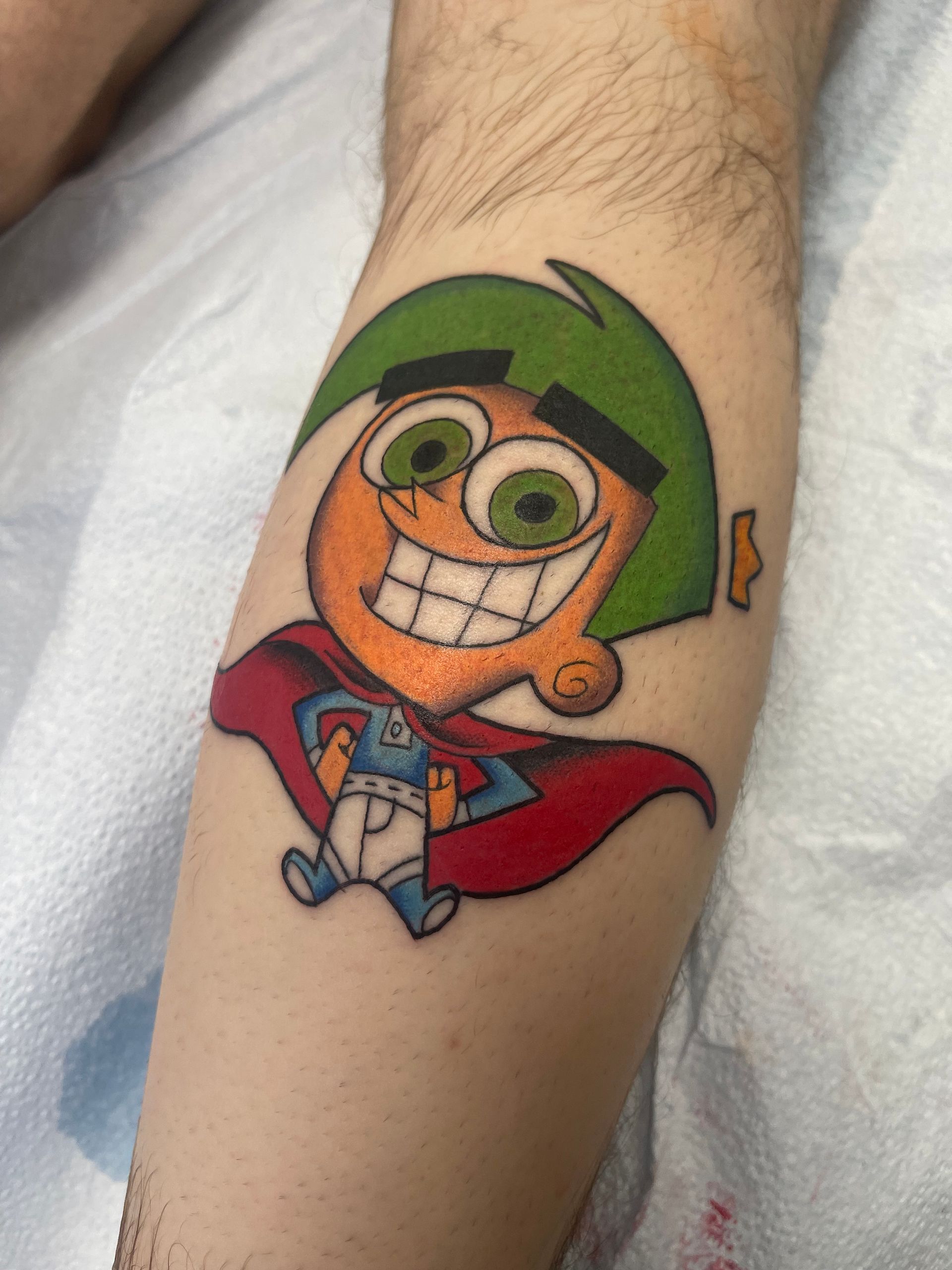 Tattoo of Cosmo from The Fairly OddParents wearing a cape, on a leg, with green hair and a grin.