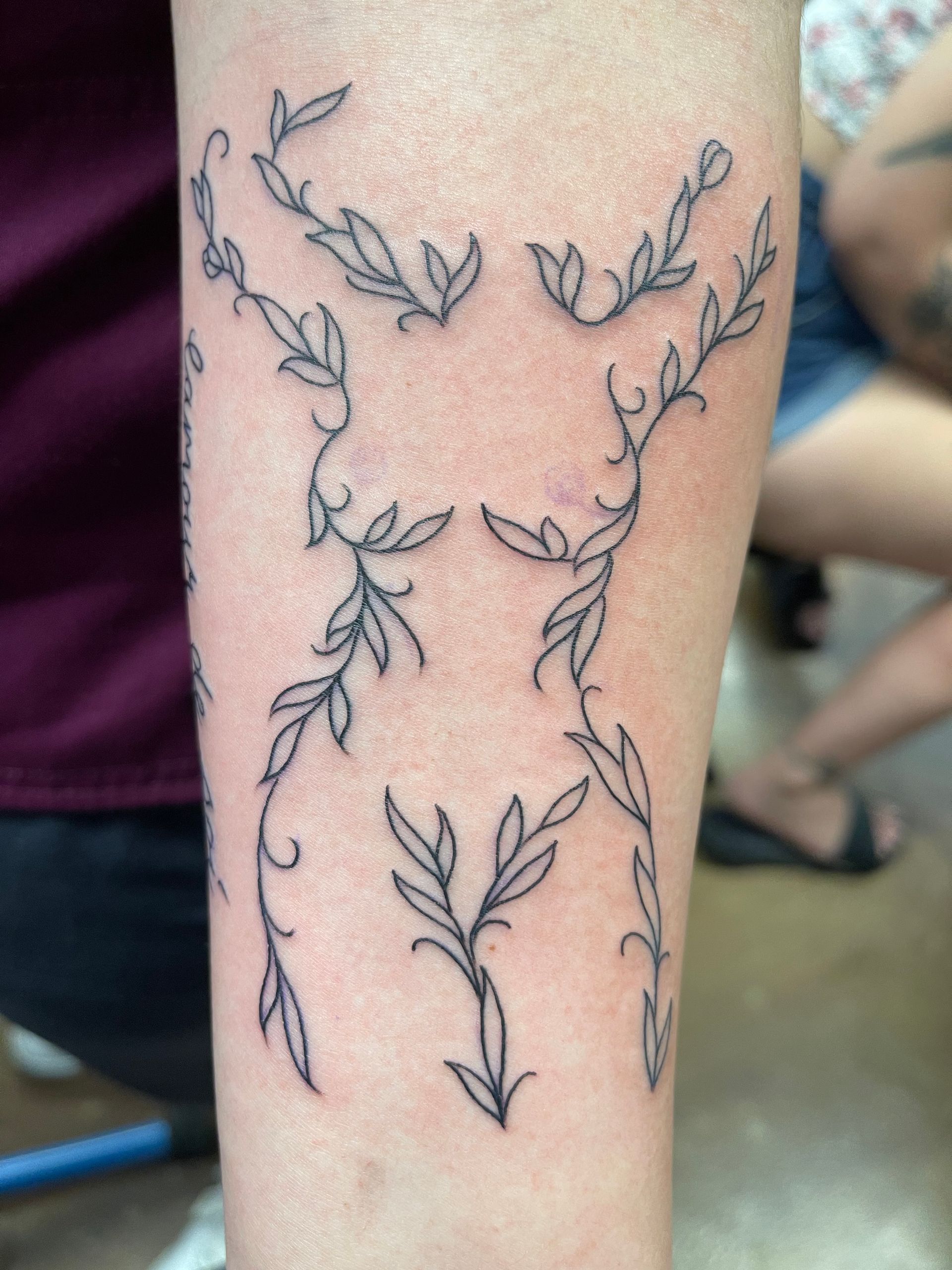 Tattoo of vine-like leaves forming a torso shape on a forearm.