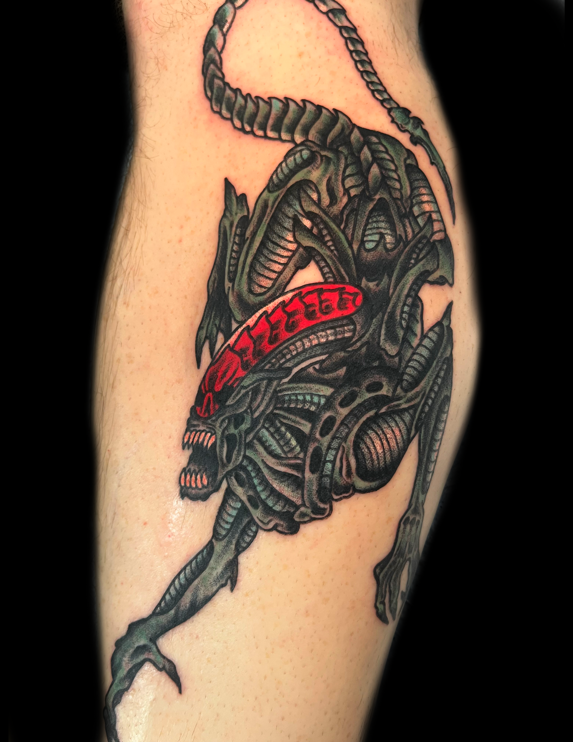 Alien tattoo in gray and red on a person's leg.