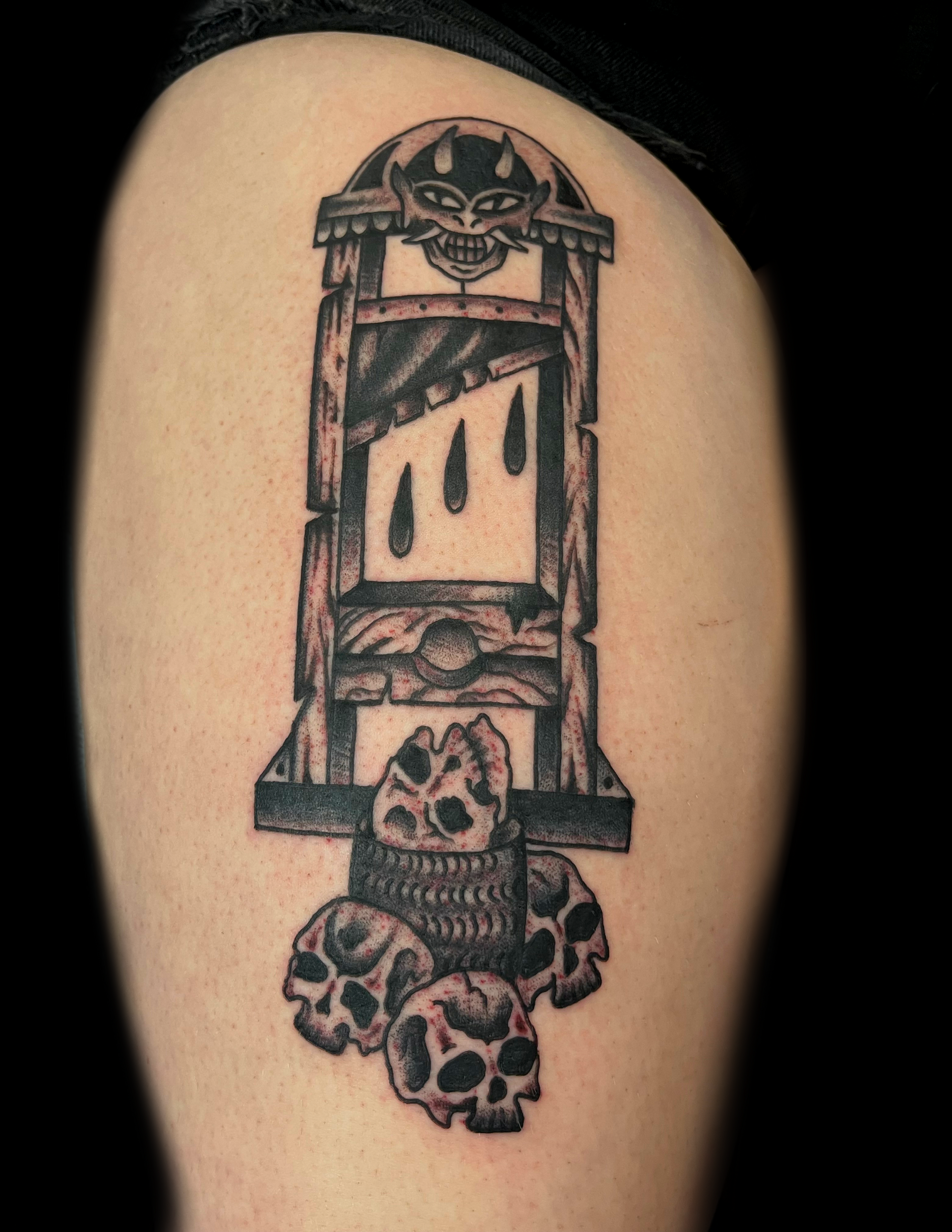 Tattoo of a guillotine with a devil face on top and skulls below. Three teardrops appear inside.