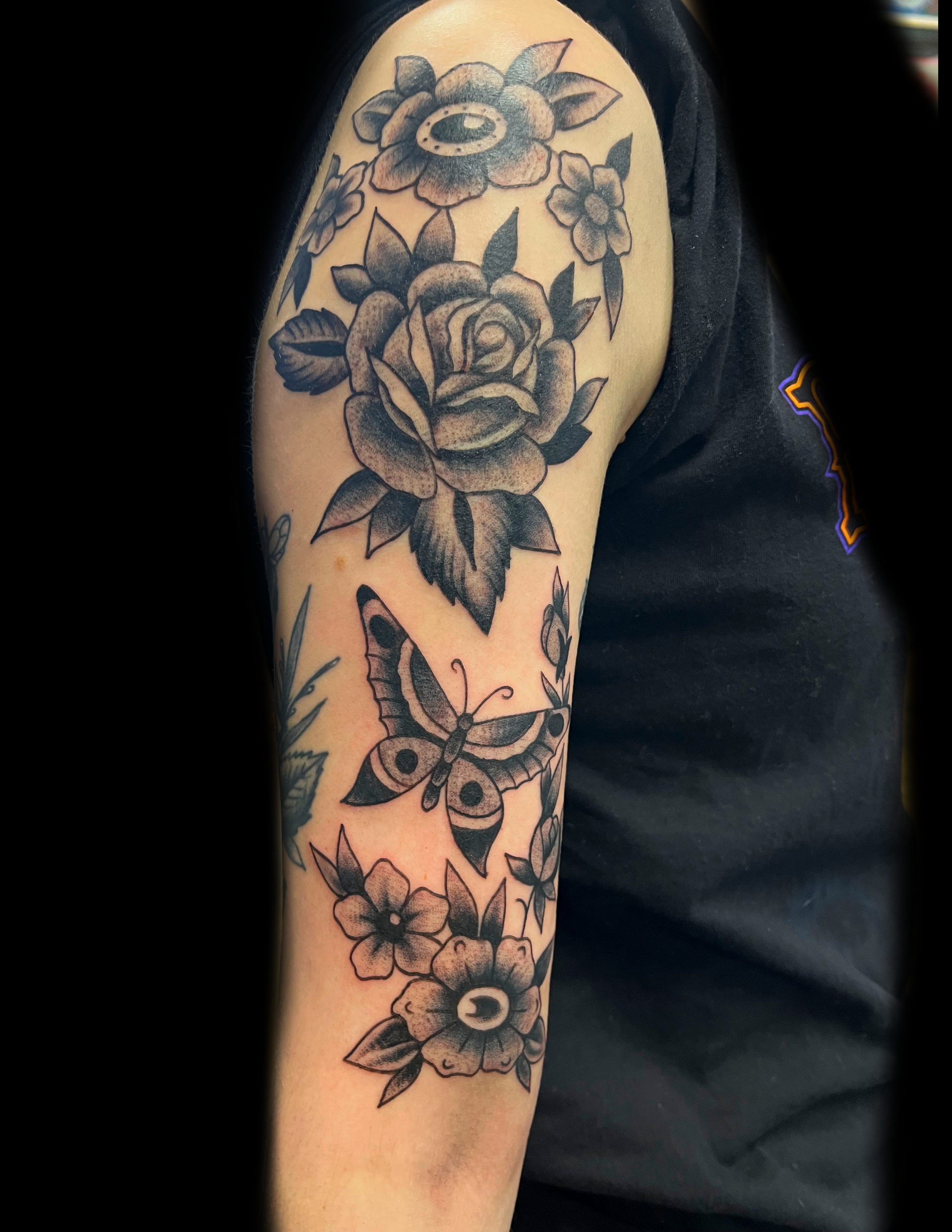 Black and gray floral and butterfly tattoo on a person's upper arm.