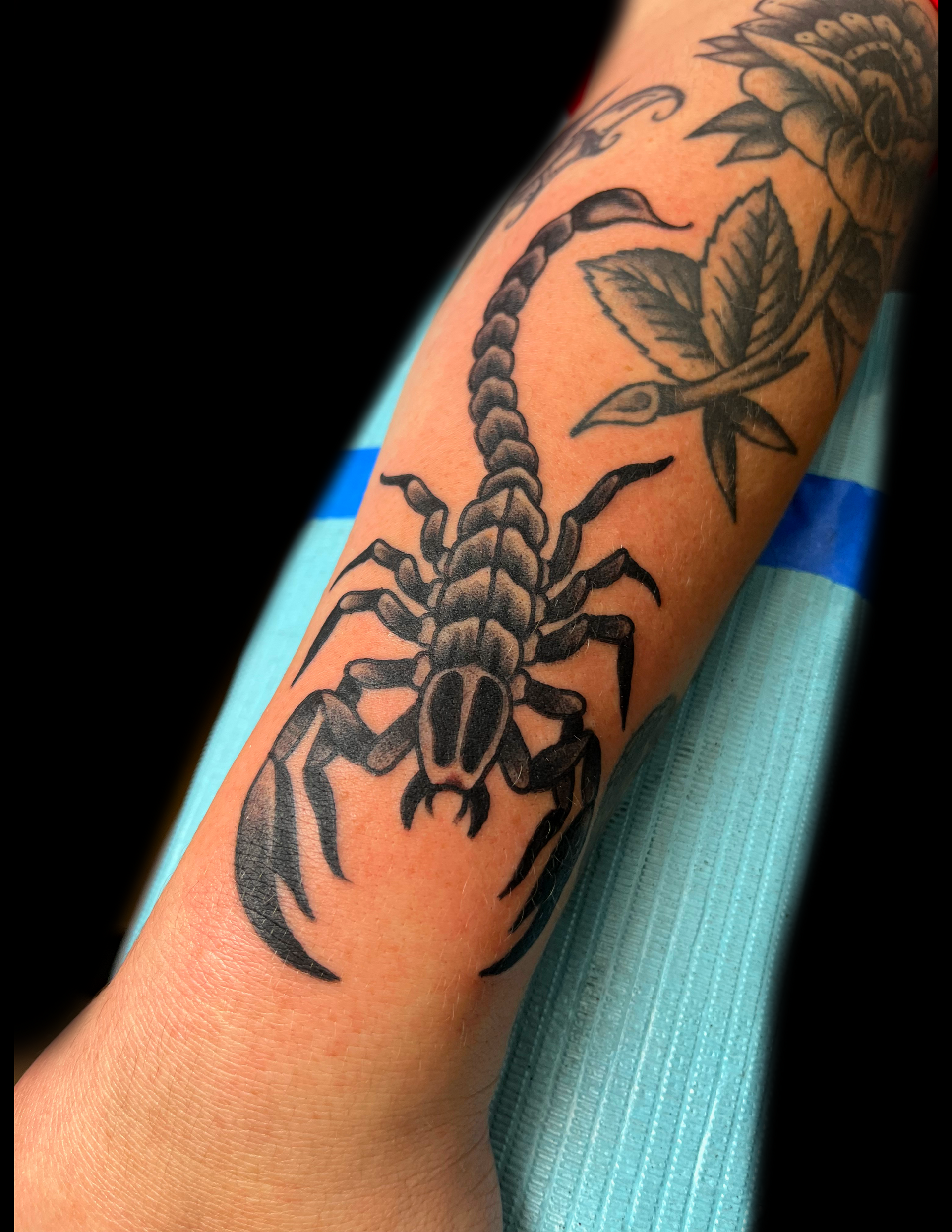 Black scorpion tattoo on arm, with floral tattoo partially visible.