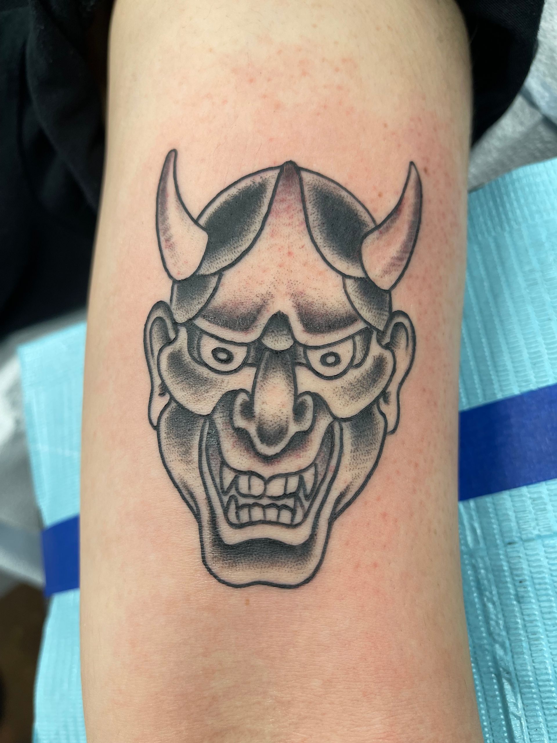 Black and gray Hannya mask tattoo on an arm, showing details of face and horns.