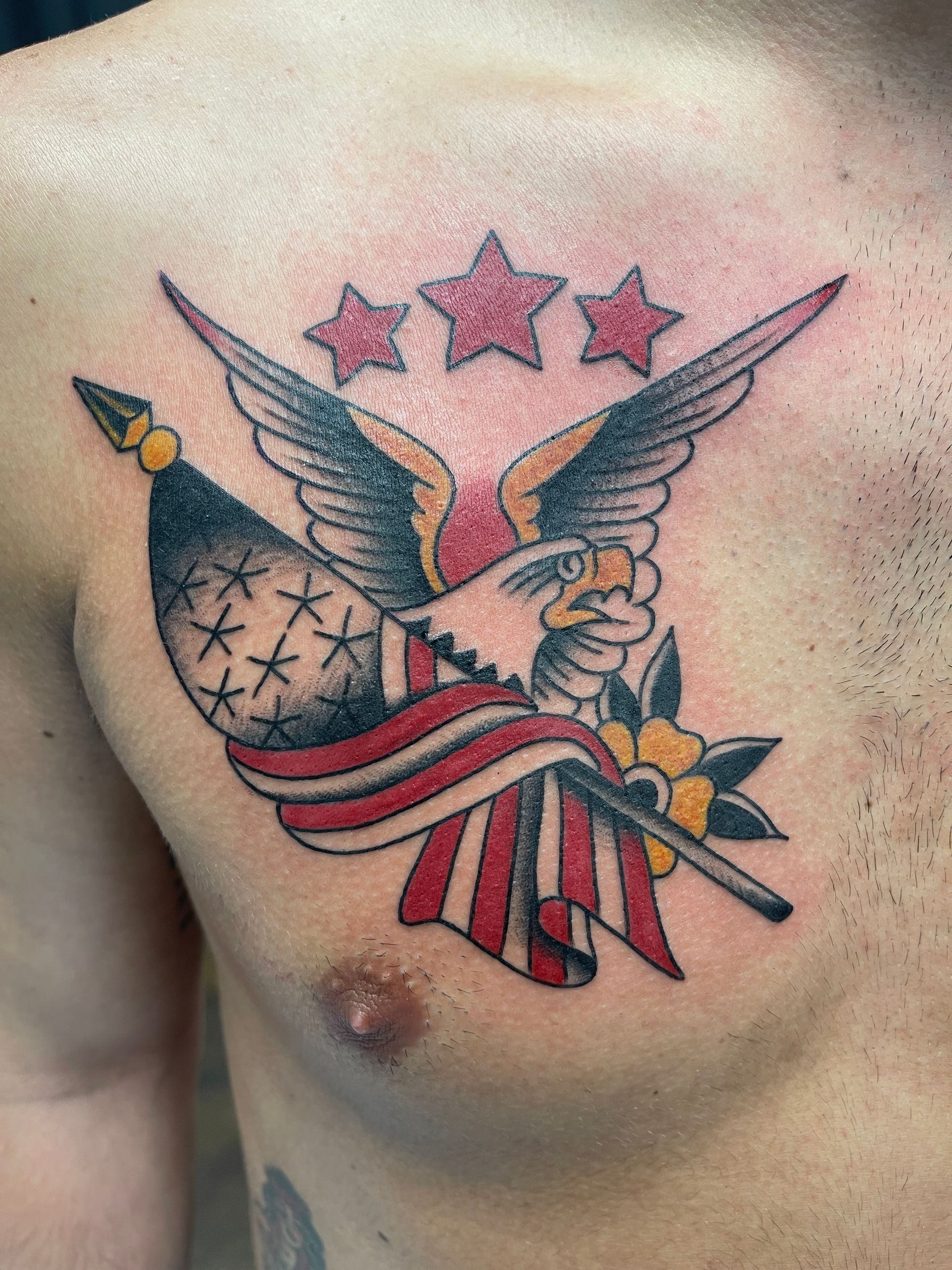 Tattoo of an eagle holding an American flag and three stars on a person's chest, red, white, and black colors.