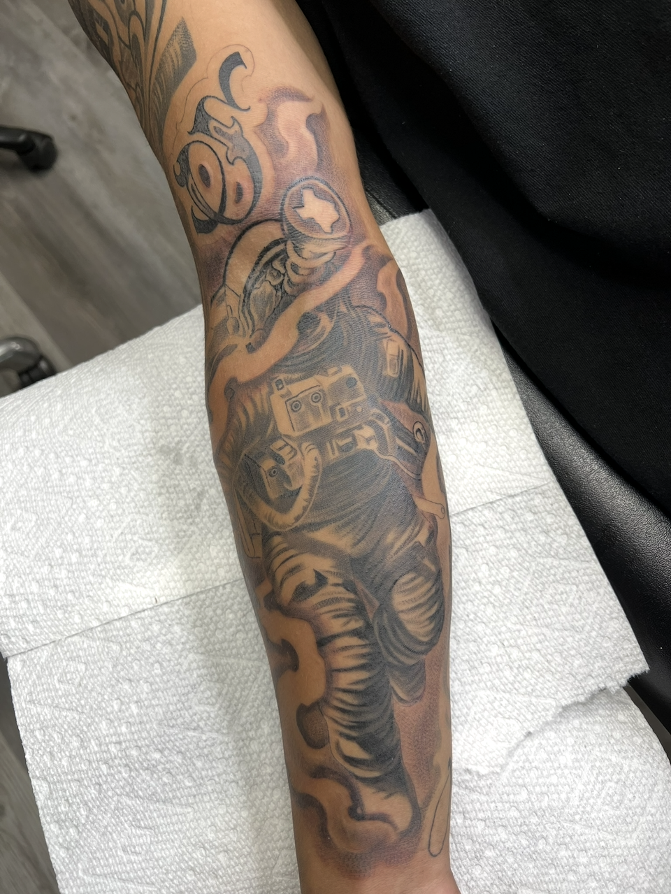 Close-up of a forearm covered in a detailed black-and-gray tattoo, resting on a white textured surface.