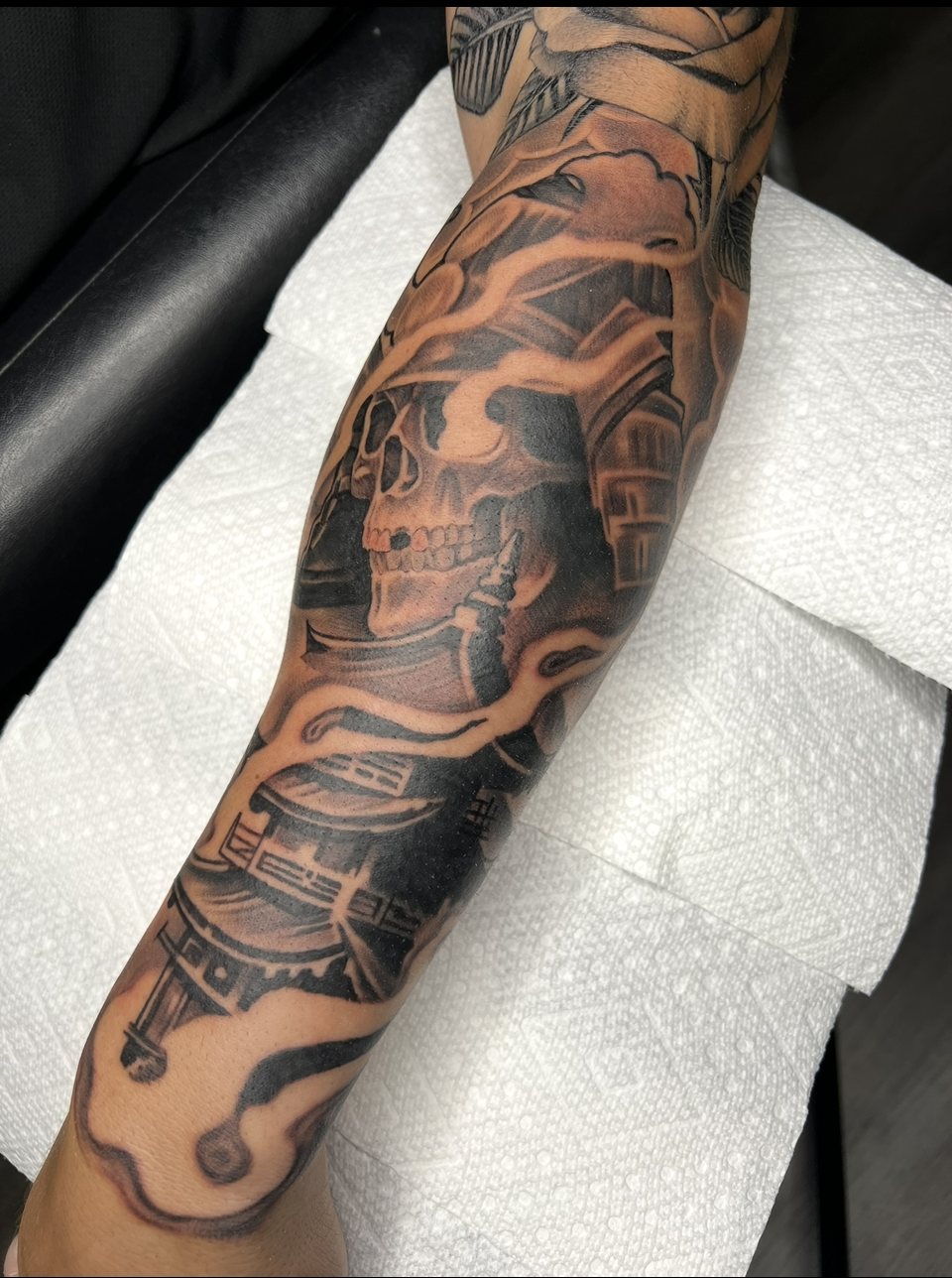 Tattooed forearm resting on white paper, showing a black and gray sleeve tattoo.