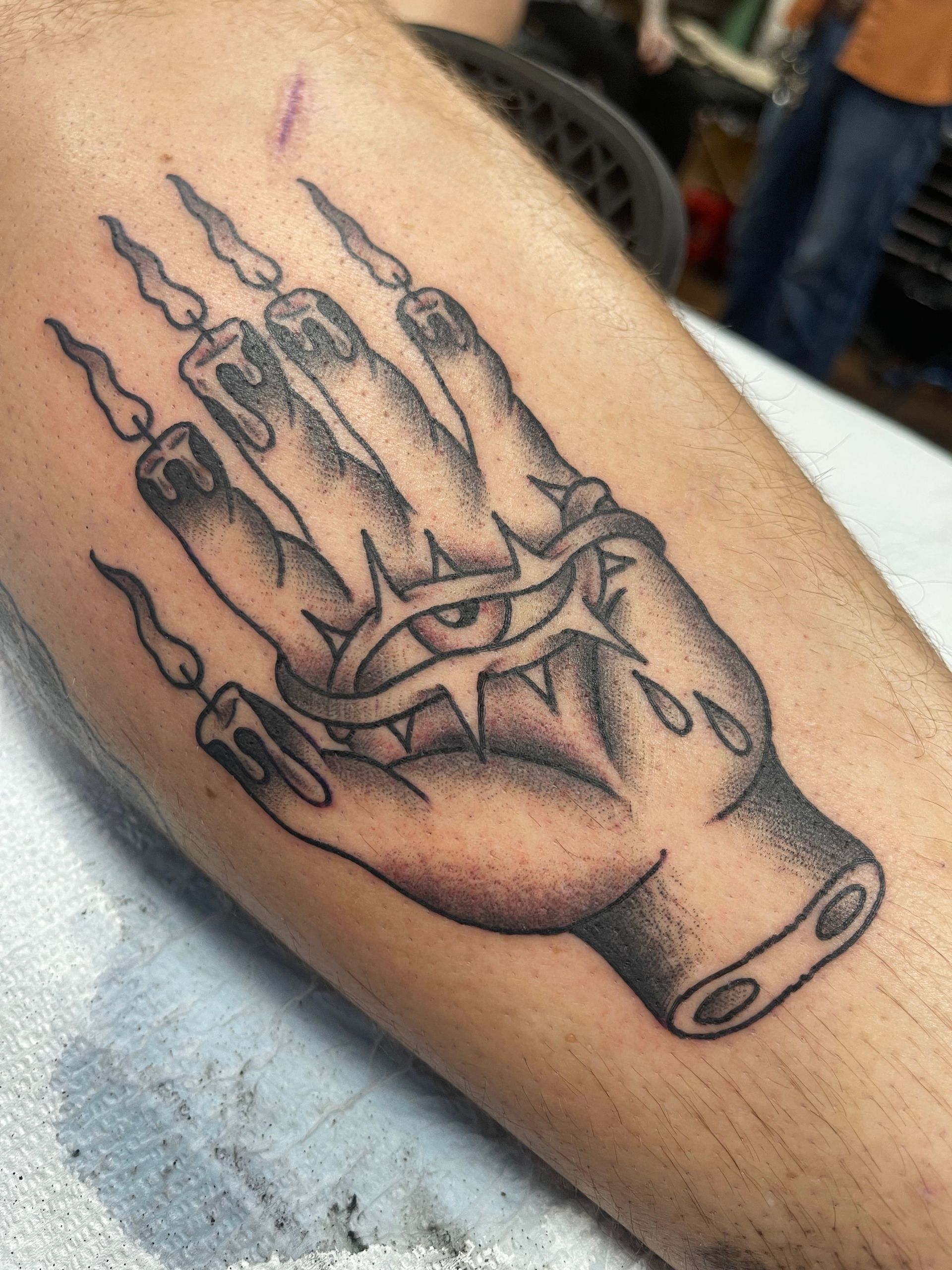 Tattoo of a hand with candles for fingers, an eye wearing a thorn crown, and water drops.