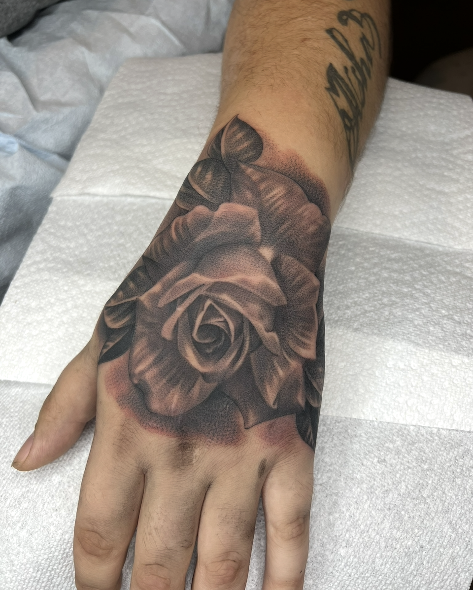 Hand with a large black rose tattoo across the back of the hand and wrist.