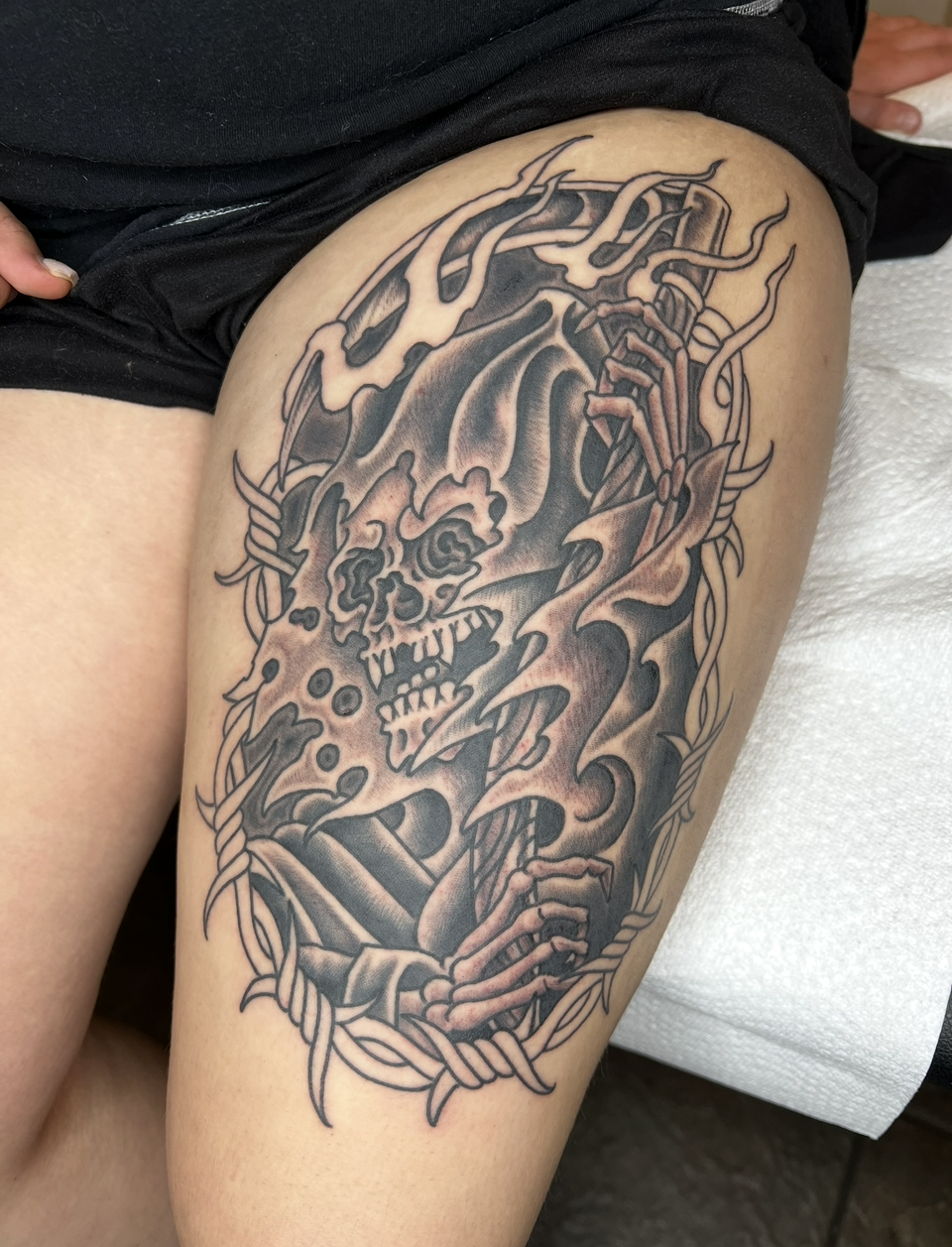 Black-and-gray skull and flames tattoo on a person’s thigh