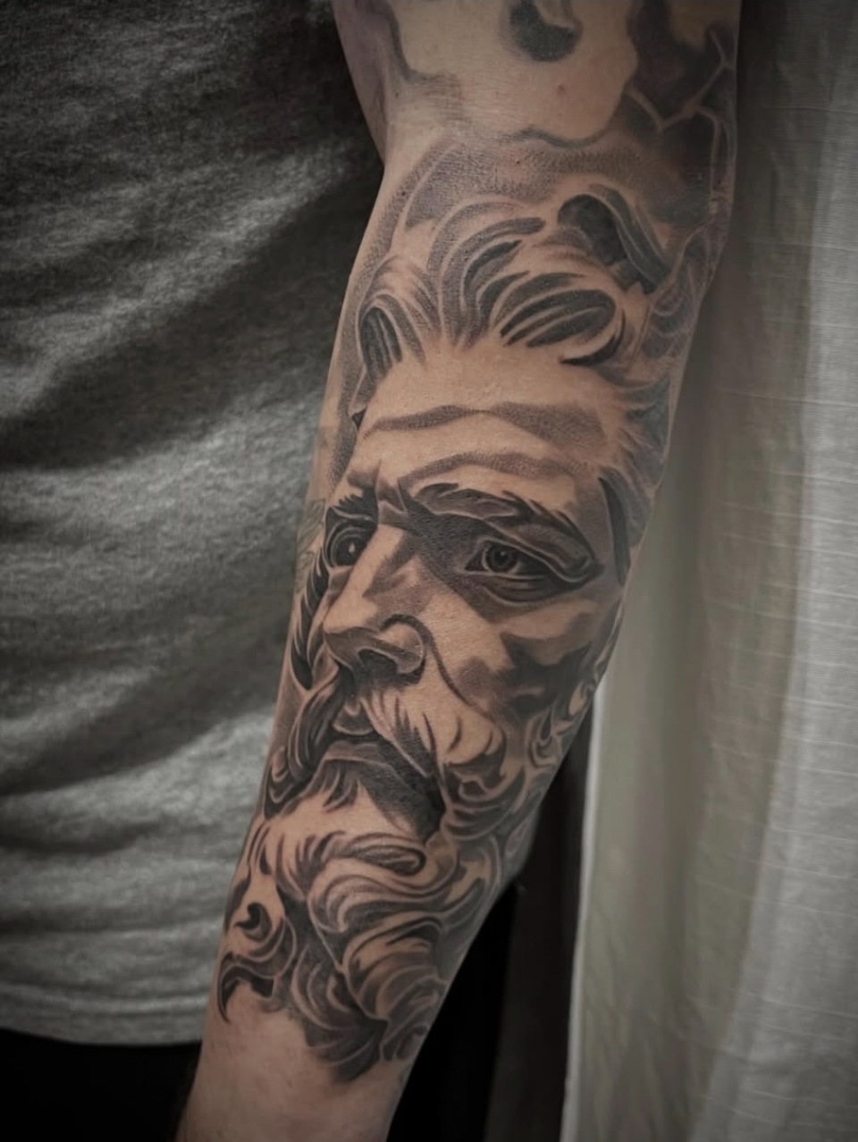 Black-and-gray tattoo of a bearded face on an upper arm