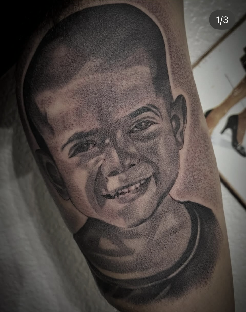 Black-and-gray tattoo portrait of a smiling child on skin
