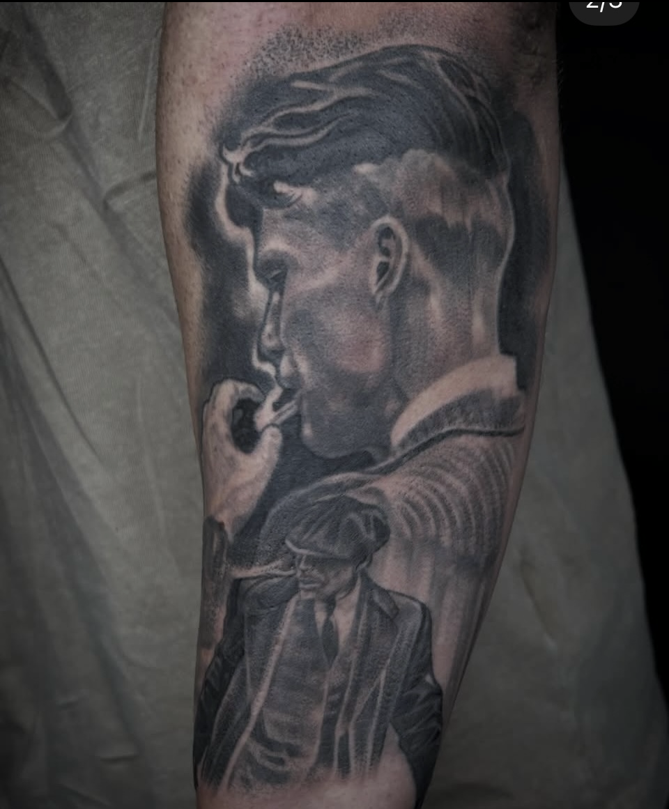 Black-and-gray tattoo of a man in profile smoking, with a detailed classical statue below on a forearm