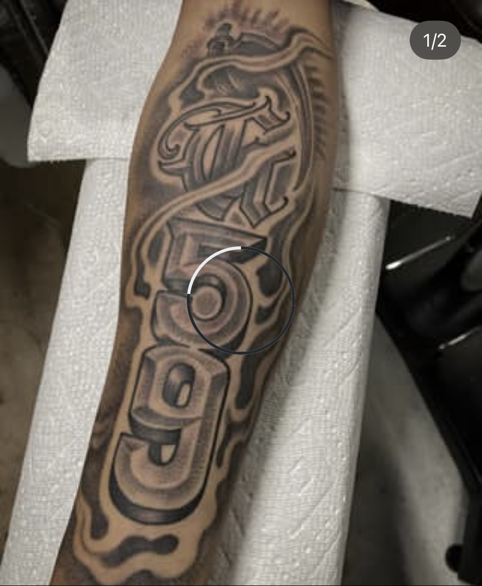 Black and gray tattoo on a forearm, featuring a stylized skull and flowing tribal patterns.