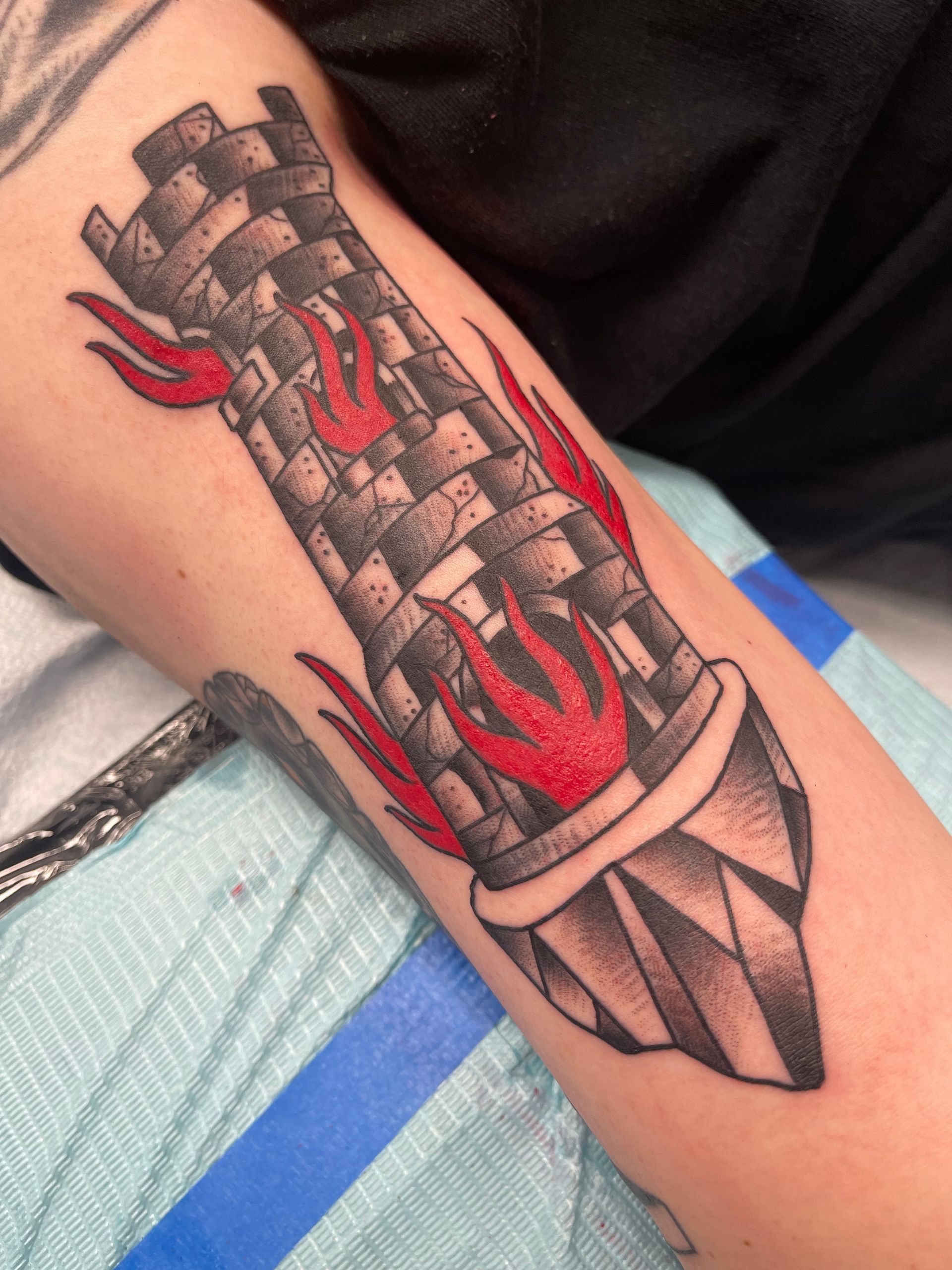 Tattoo of a checkered tower with red flames on an arm.