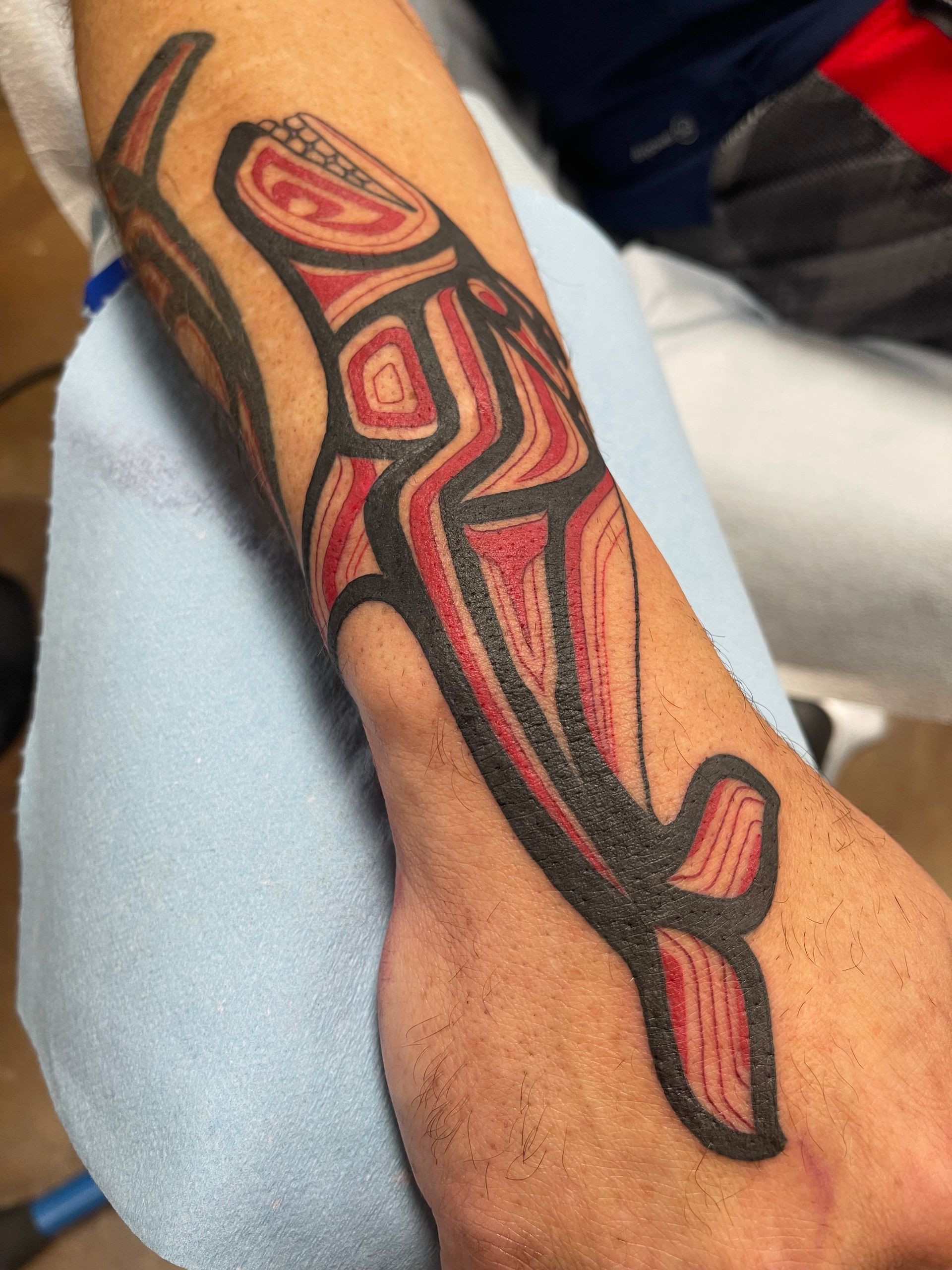 Tattoo of a stylized orca whale in red and black ink on a person's wrist.