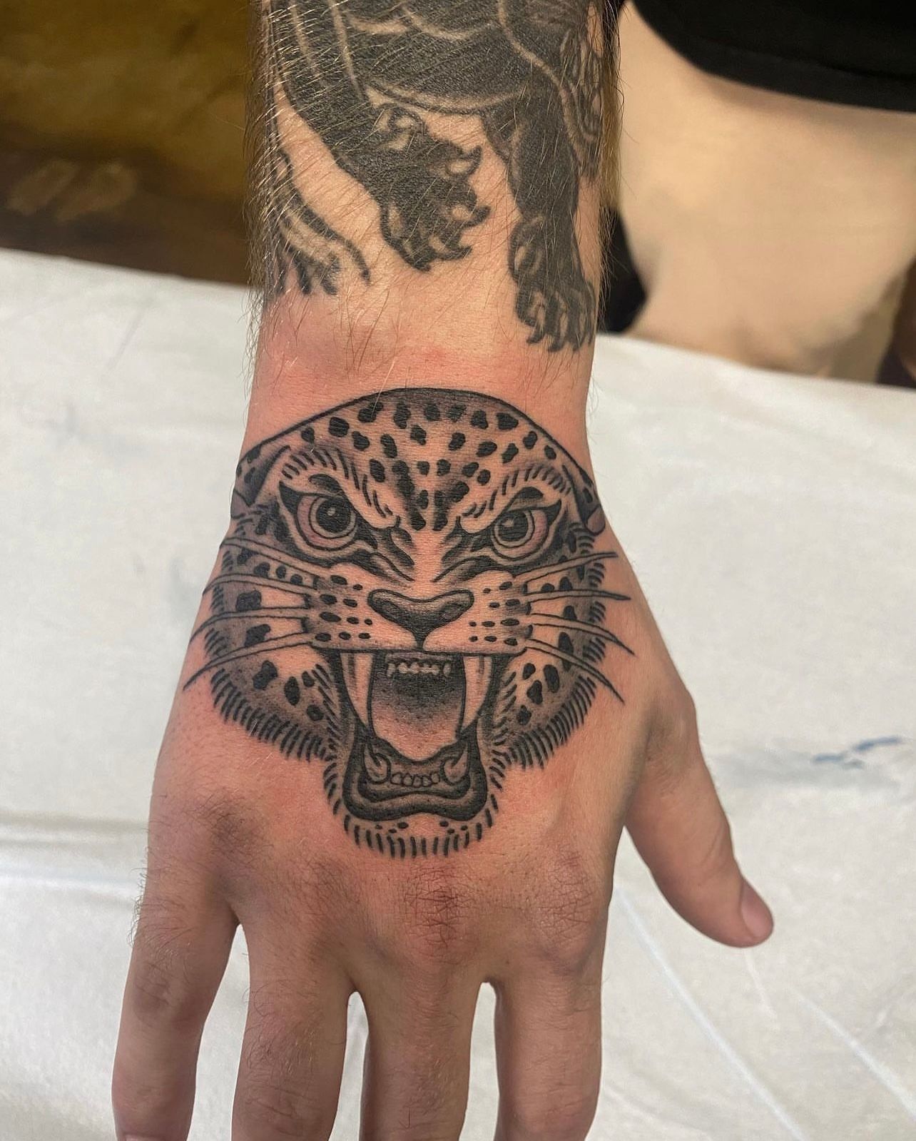 Tattoo of a leopard's snarling face on a hand, with spots, sharp teeth, and detailed shading.