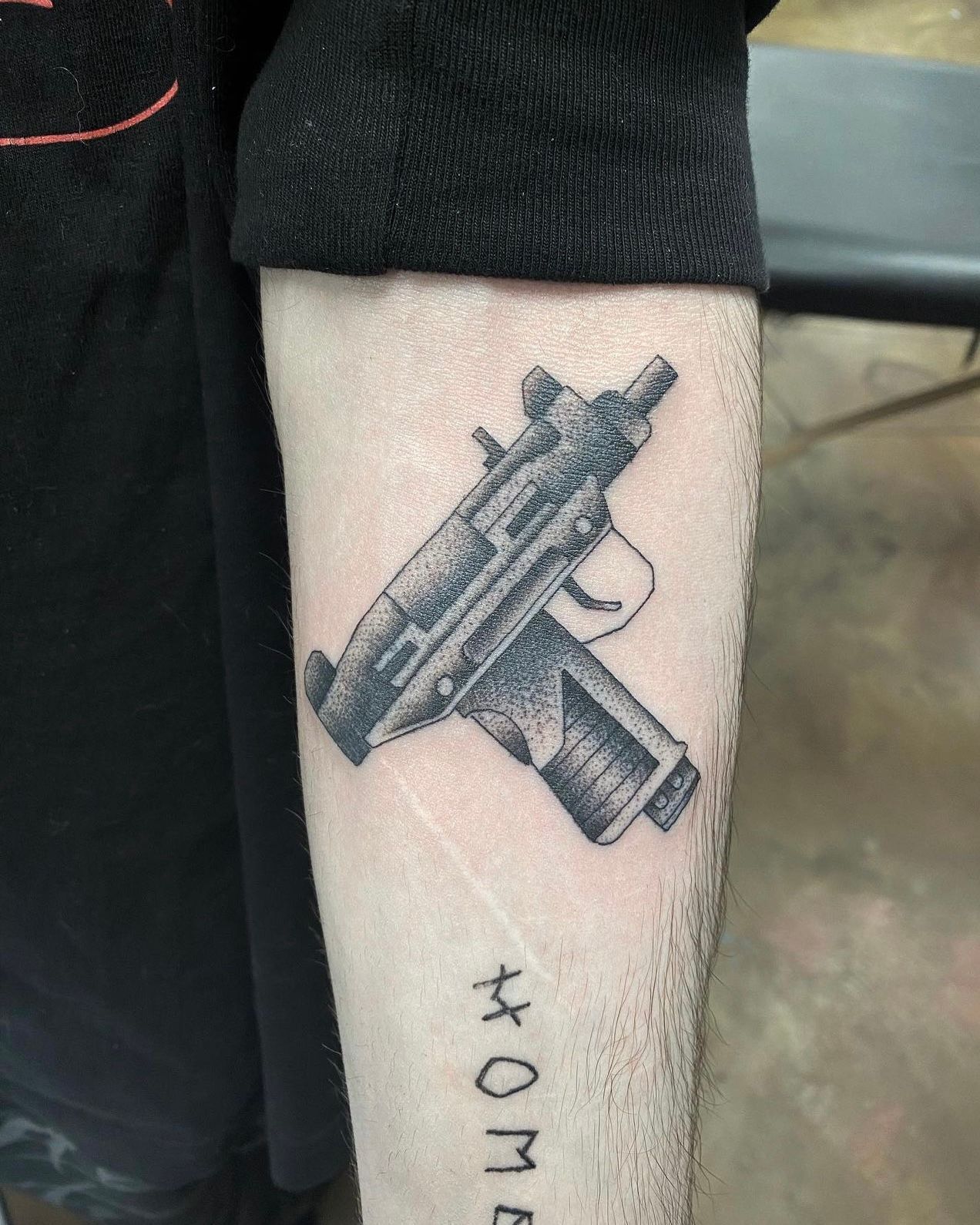 Tattoo of an Uzi submachine gun on a forearm. The word 