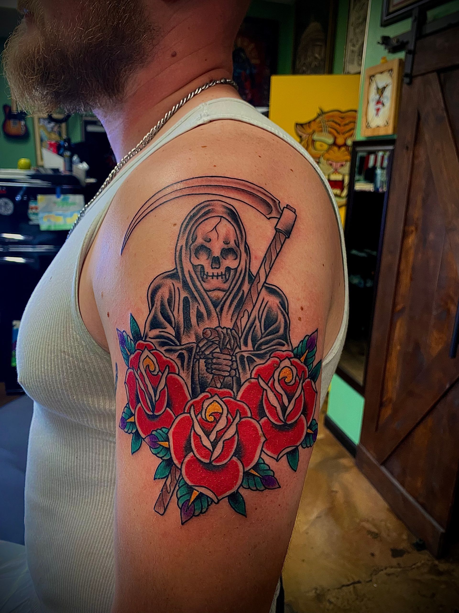 Tattoo of Grim Reaper with scythe, surrounded by red roses on a person's upper arm.
