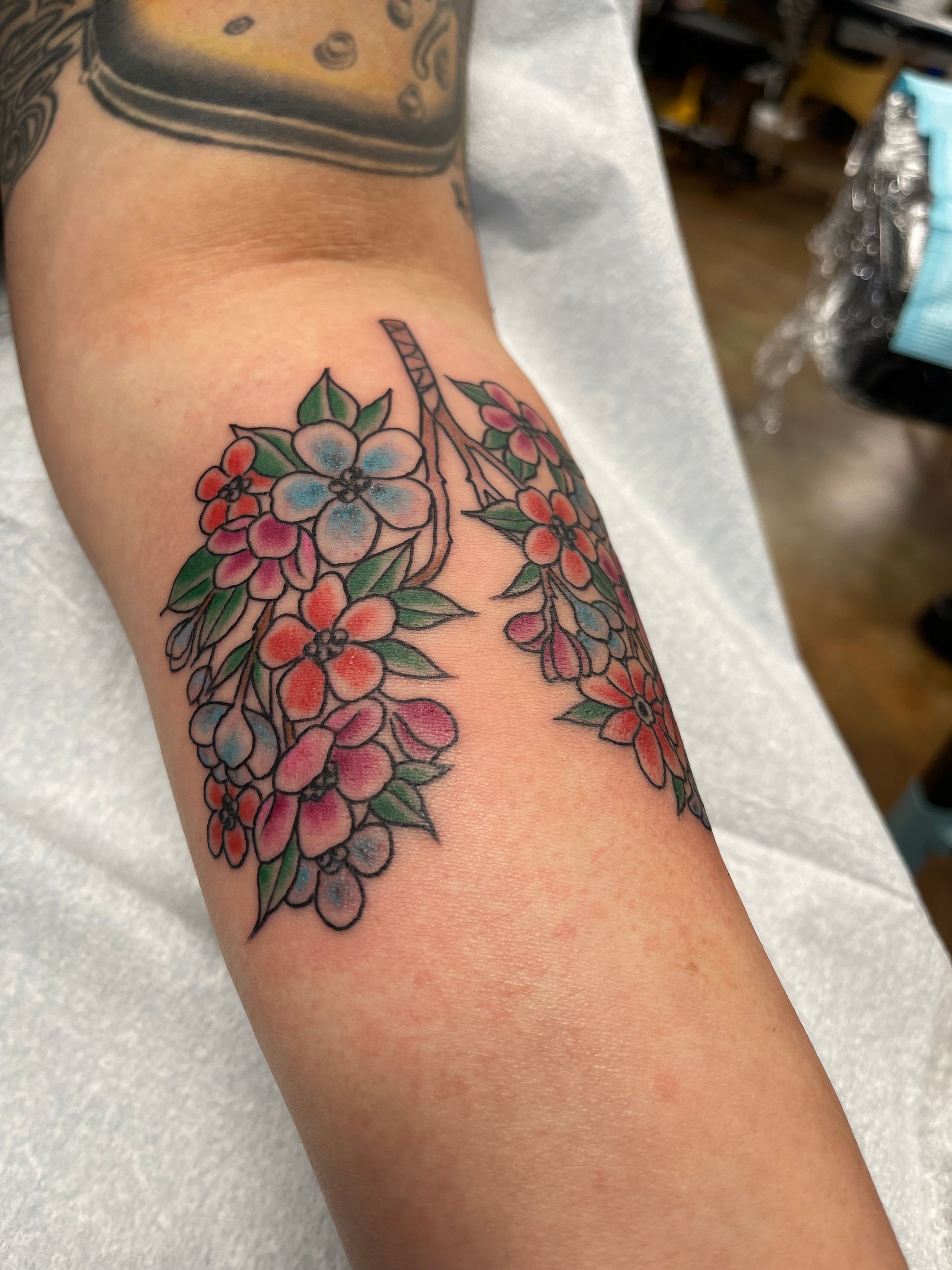Tattoo of floral lungs on an arm, with pink, blue, and orange flowers, green leaves.