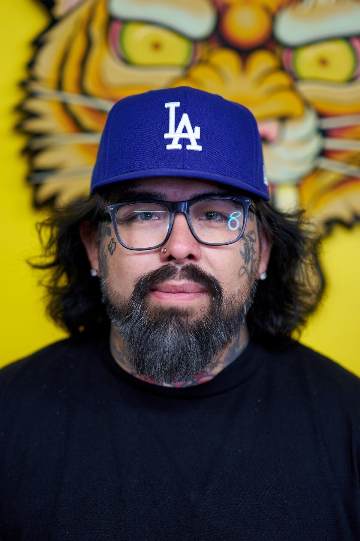 Man in a blue LA cap and glasses against a yellow mural background
