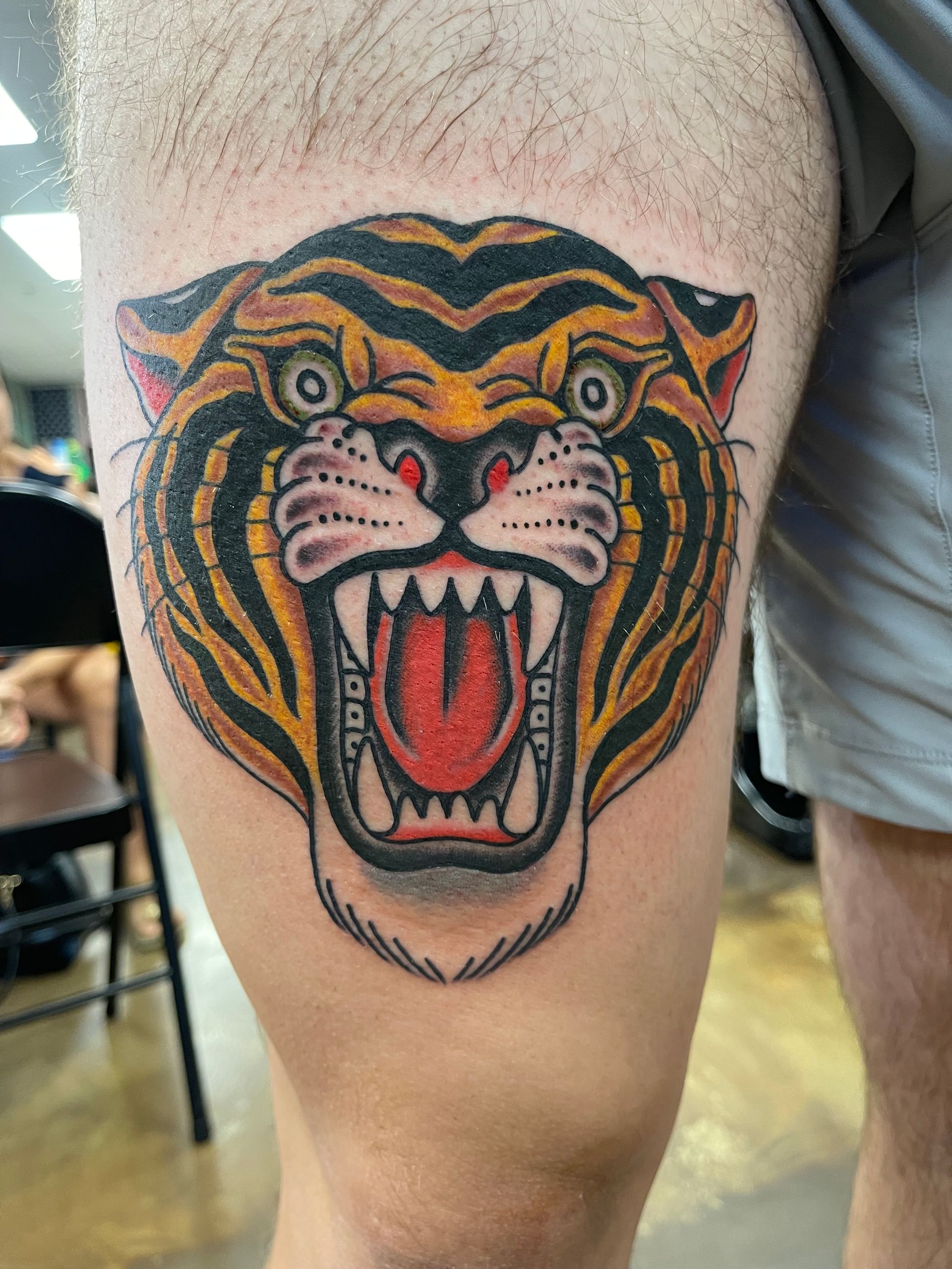 Roaring tiger head tattoo on a leg, with black, orange, and red details.