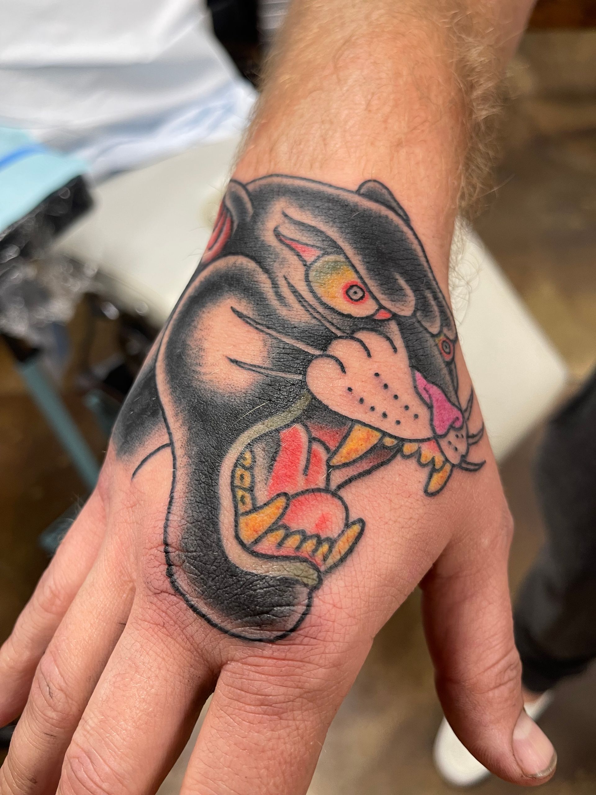 Black panther tattoo on a hand. The panther has a menacing expression with its mouth open, revealing teeth.