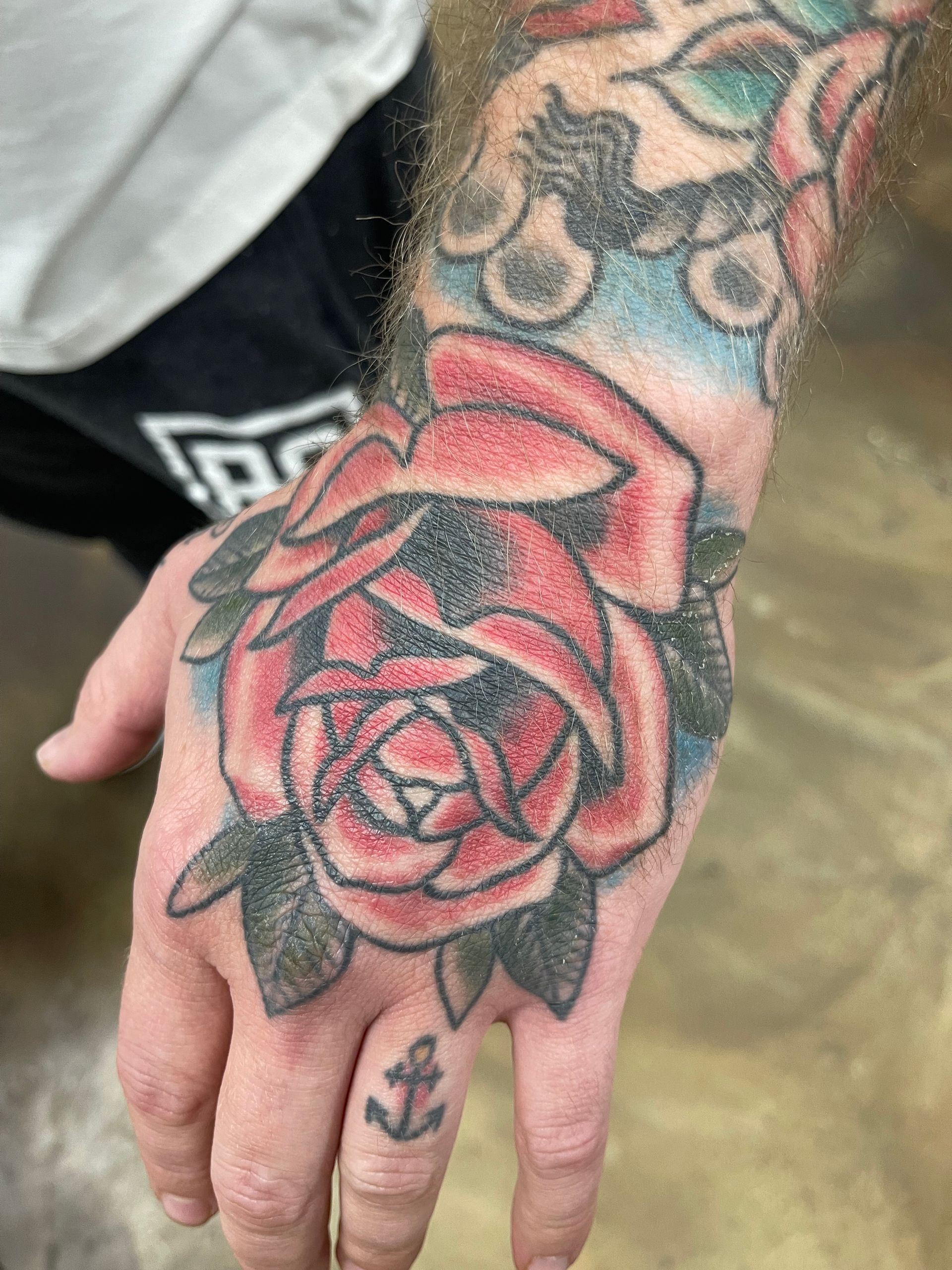 Hand with a red rose tattoo and an anchor tattoo on the finger.