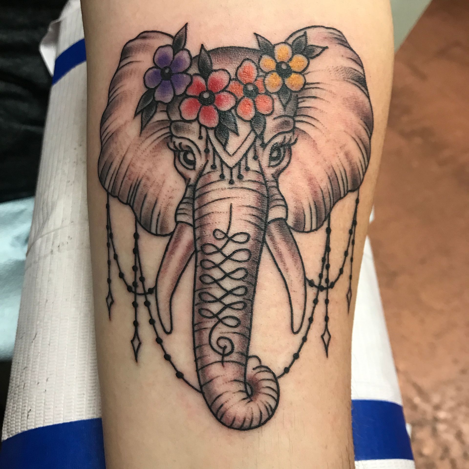Elephant tattoo with floral crown and beaded accents, on an arm.