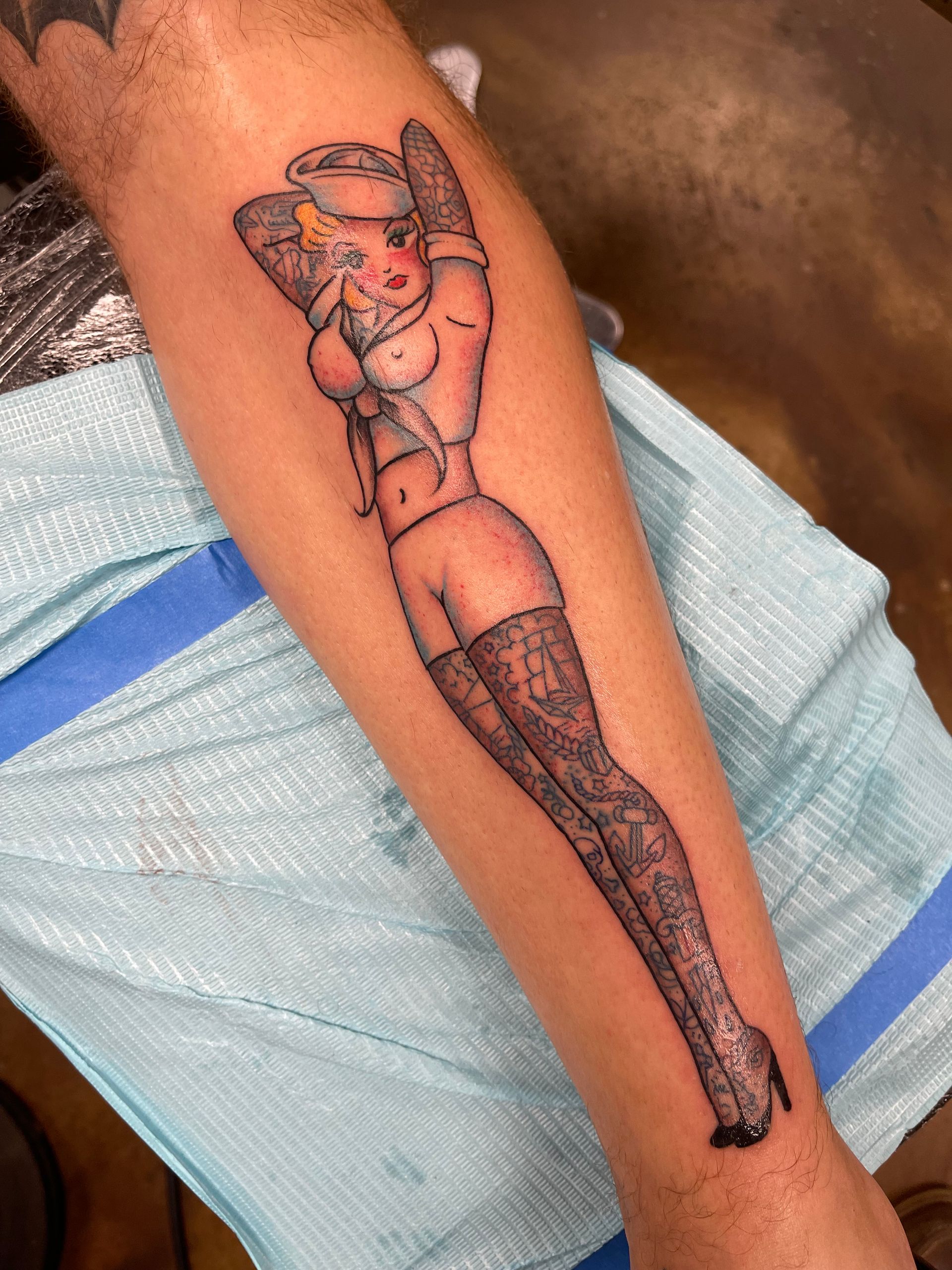 Tattoo of a pin-up girl on an arm. She wears a sailor hat, lingerie, and patterned stockings.