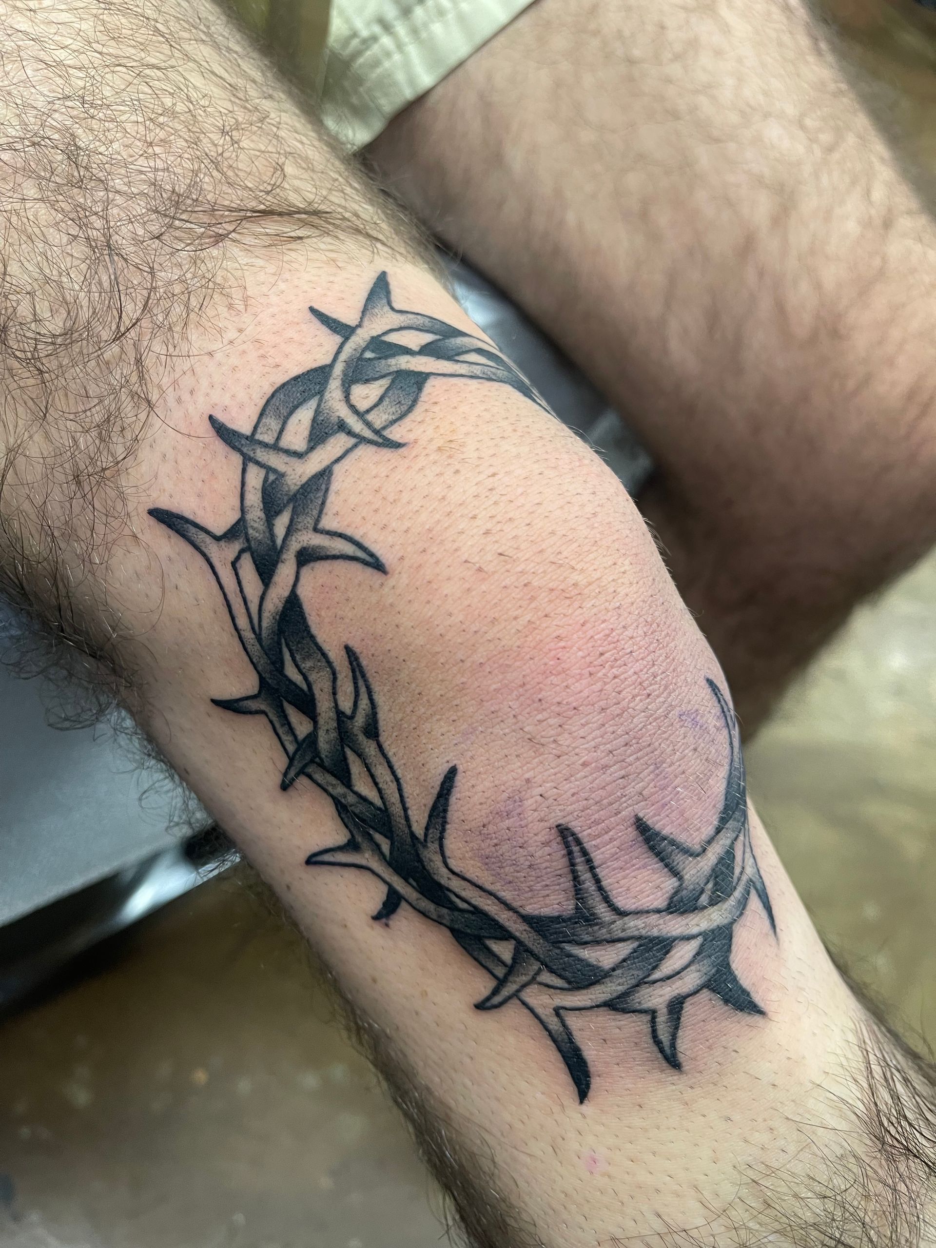 Tattoo of a black and gray crown of thorns on an arm.