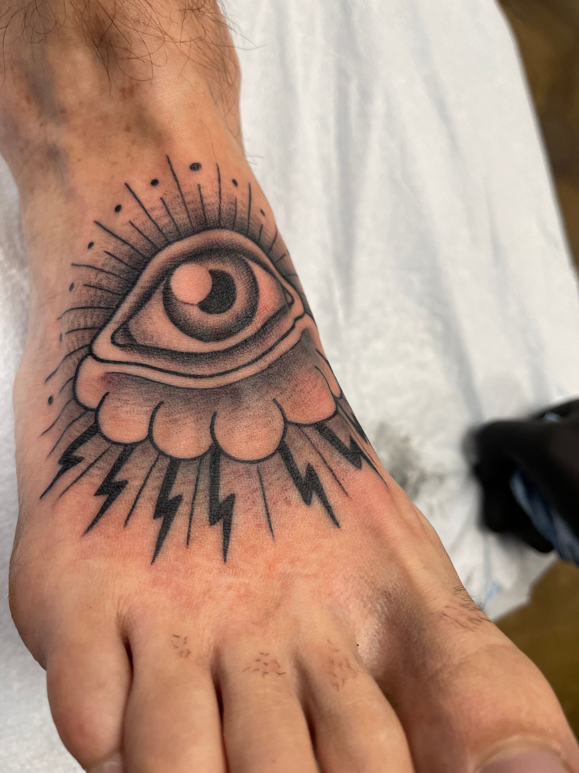 Foot tattoo of an eye with rays and lightning bolts.