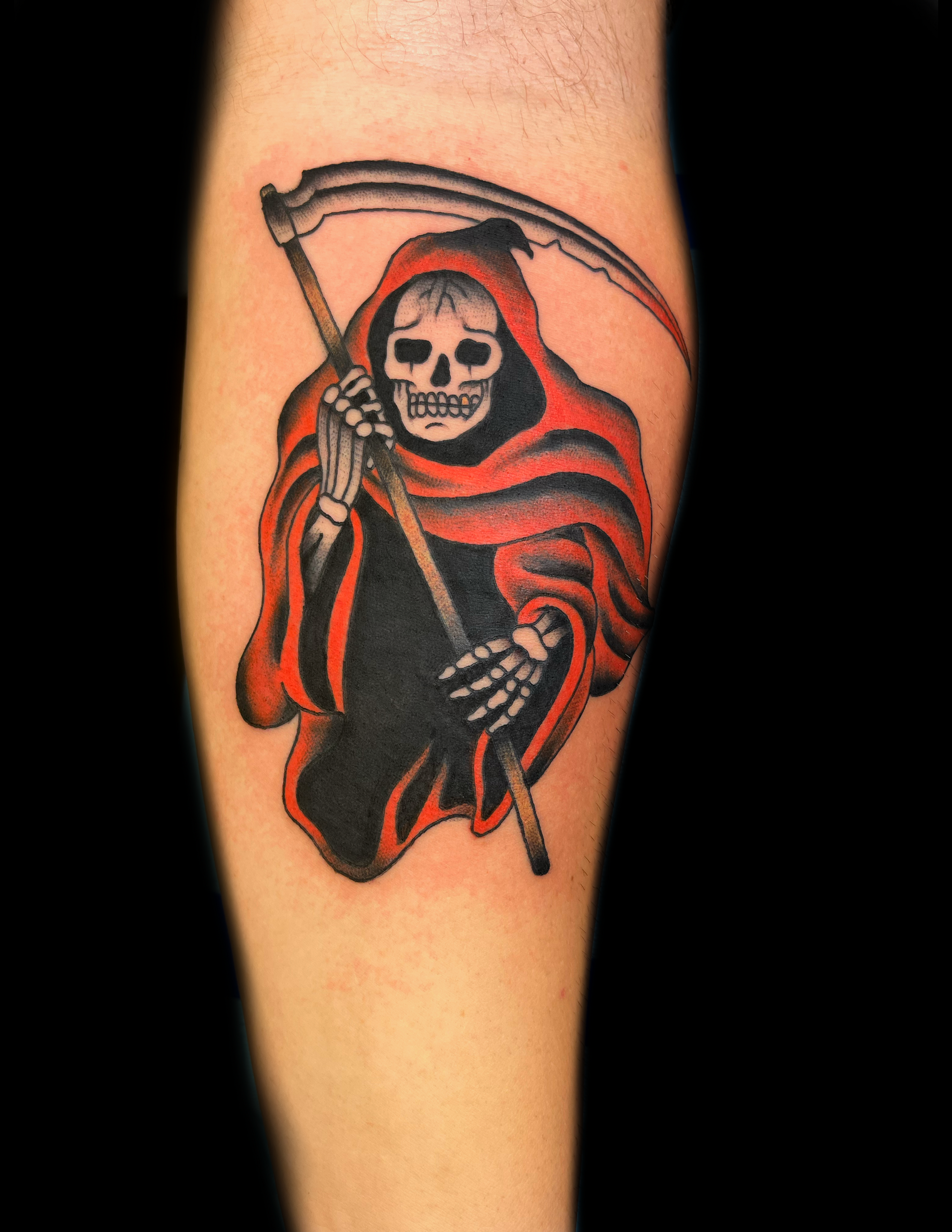 Grim Reaper tattoo on arm, red and black robes, holding a scythe.
