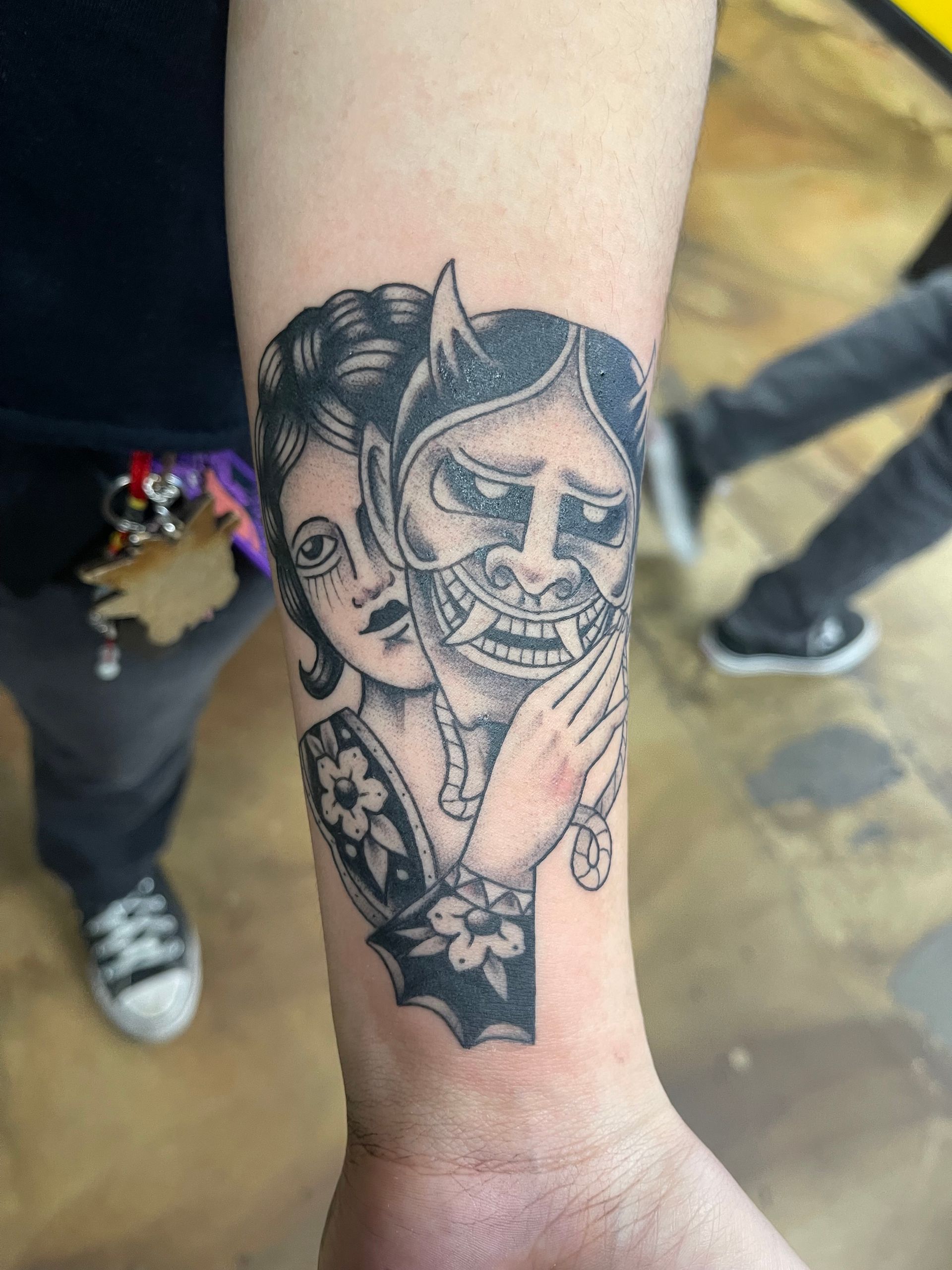 Tattoo on an arm: Woman holding a Japanese demon mask, black ink design.