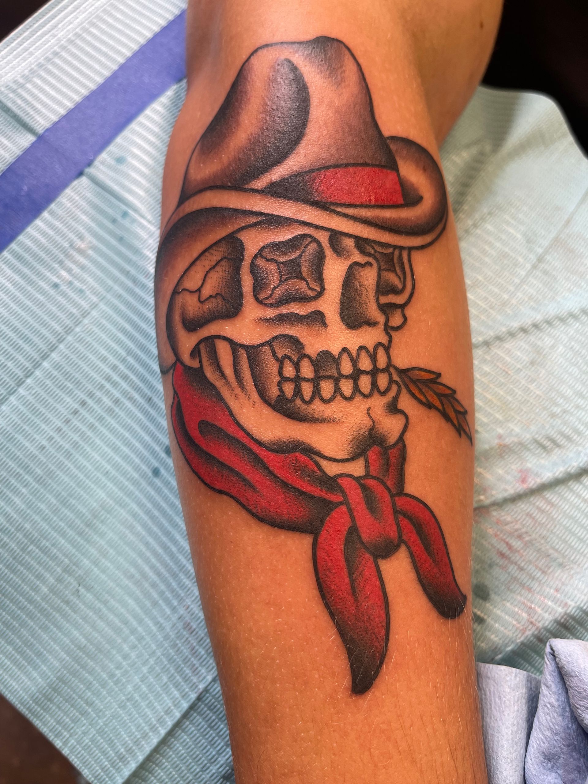 Skull tattoo with cowboy hat, red bandana, and feather on arm.