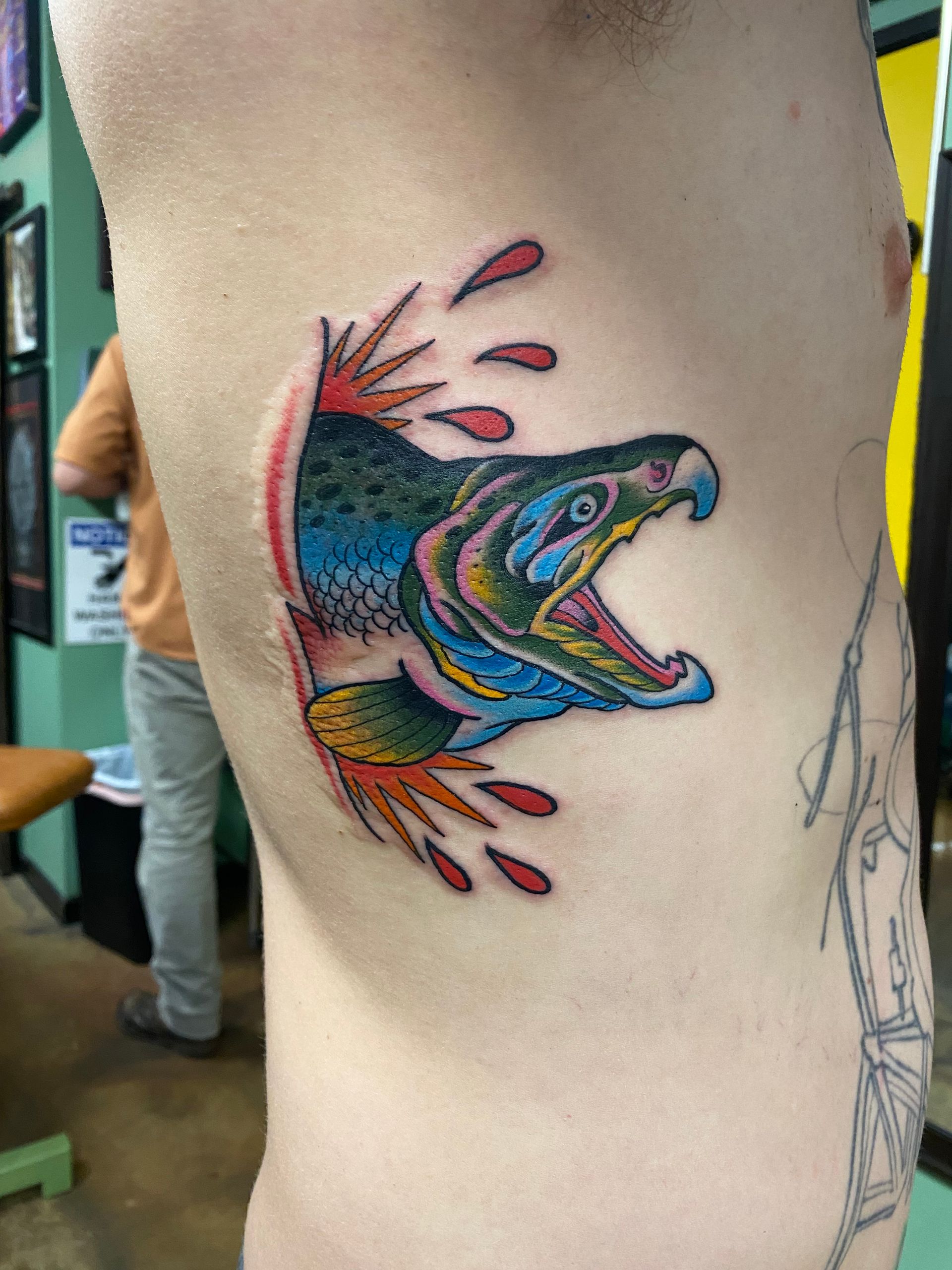 Colorful salmon tattoo bursting from skin on a person's side, mouth open.