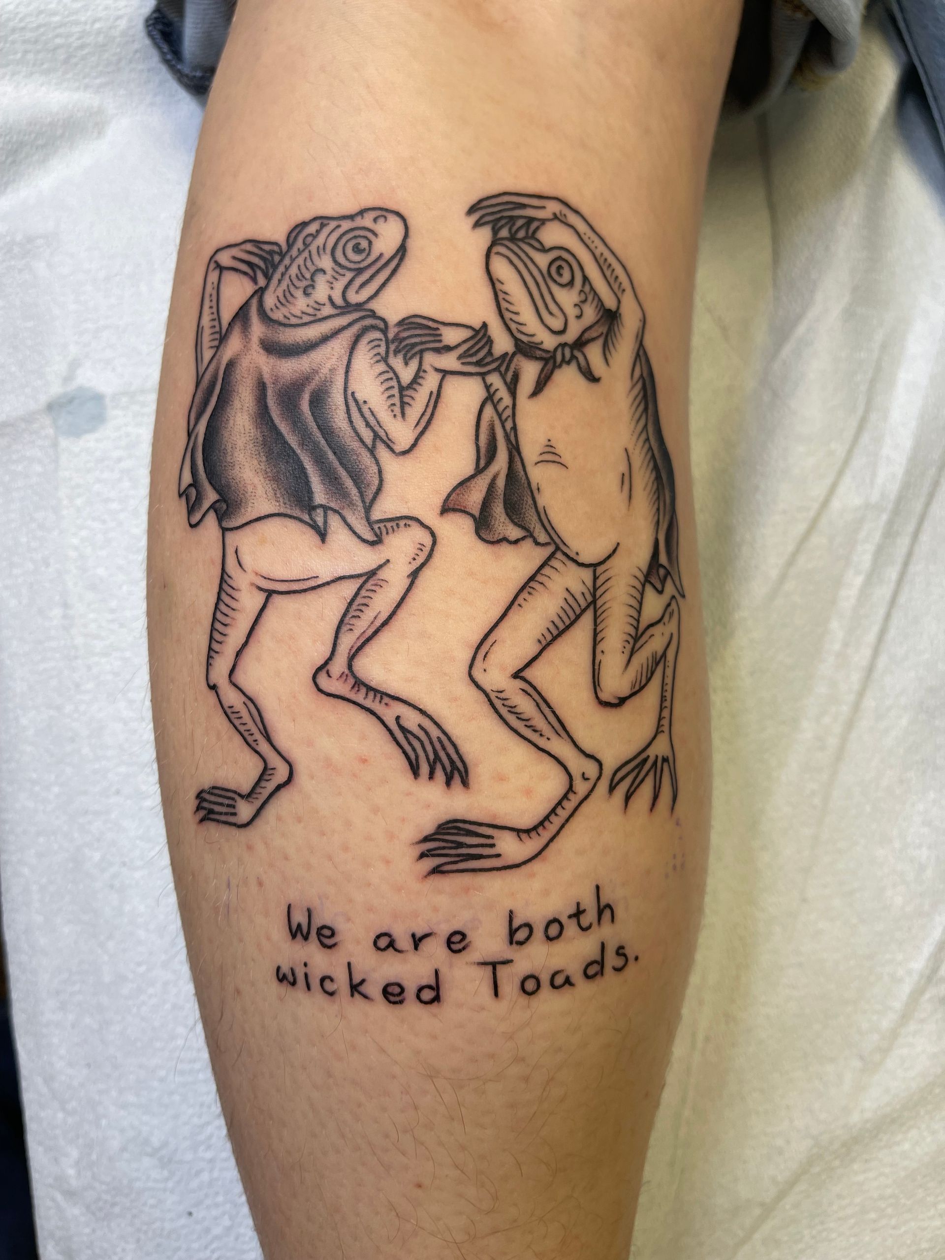 Tattoo of two cartoonish toads dancing with text: 