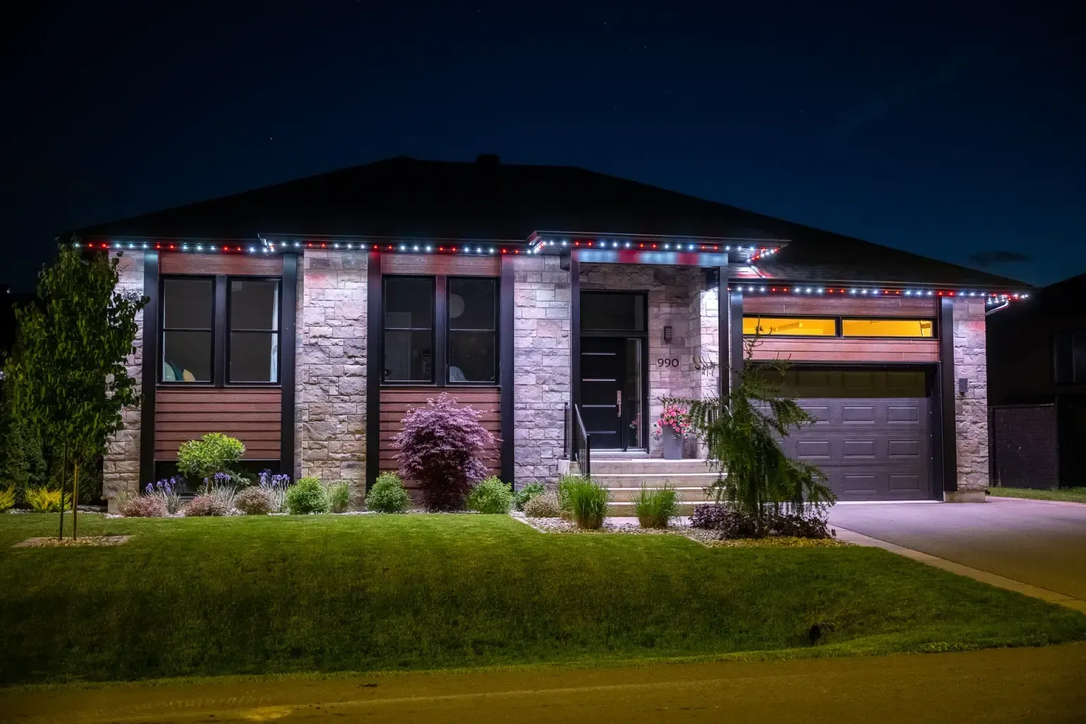 House at night, illuminated with red, white, and blue lights above windows and garage door. Green lawn.