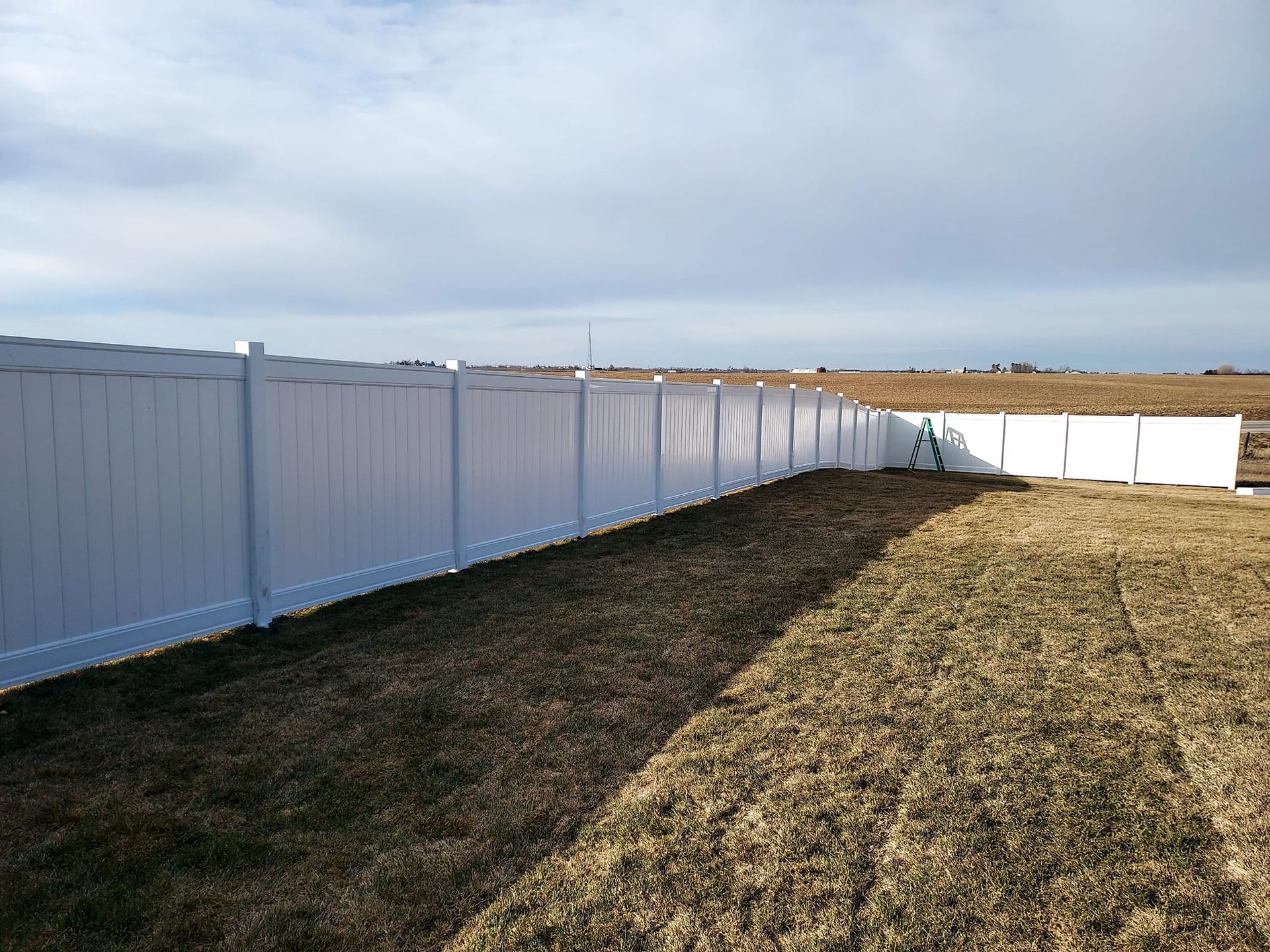 A white vinyl fence surrounds a dry grass field.