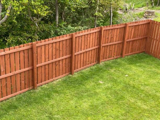 A wooden fence surrounds a lush green lawn in a backyard.