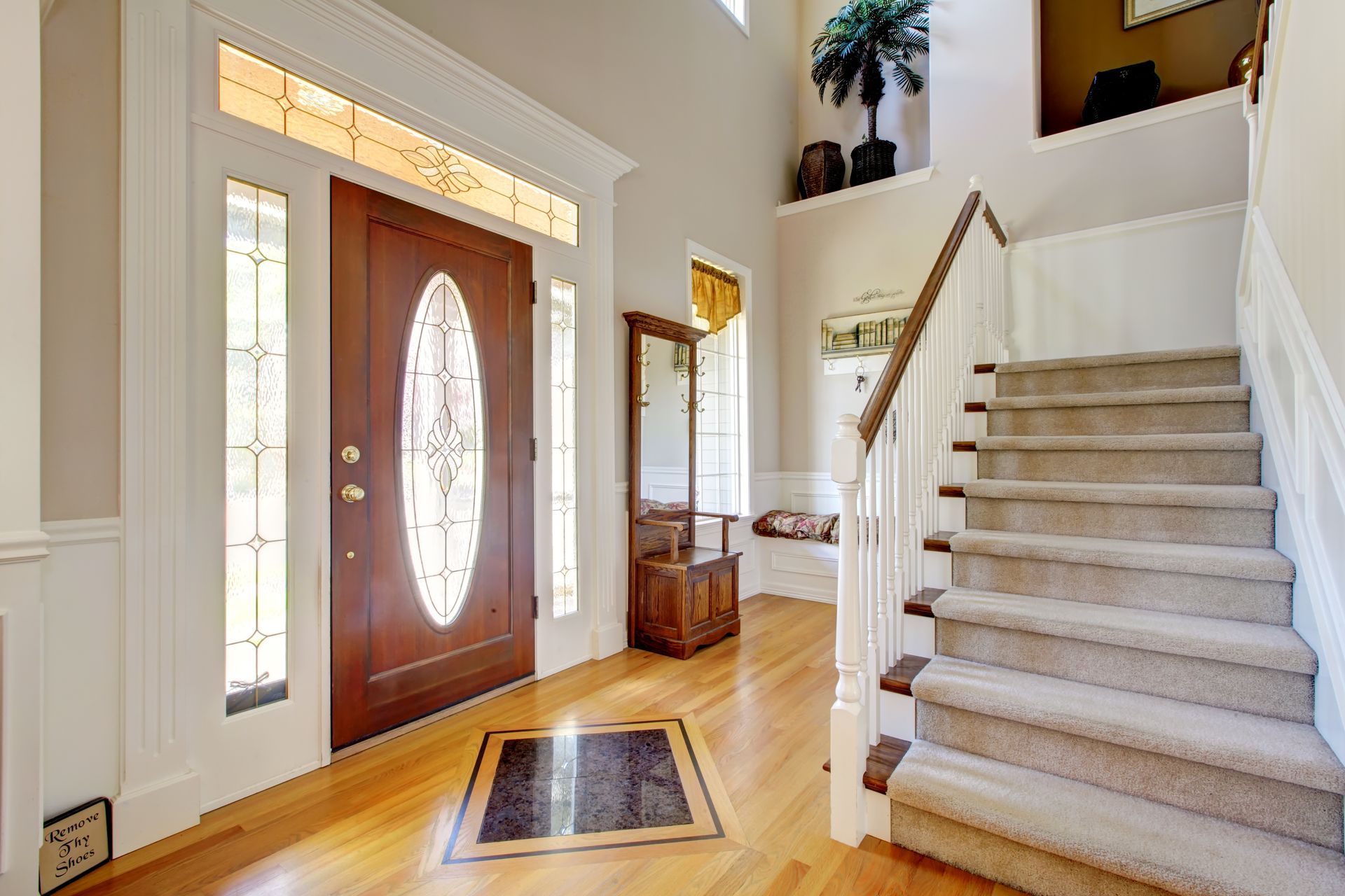 Bright foyer with front door, staircase, and tile and wood flooring, lit by tall windows.