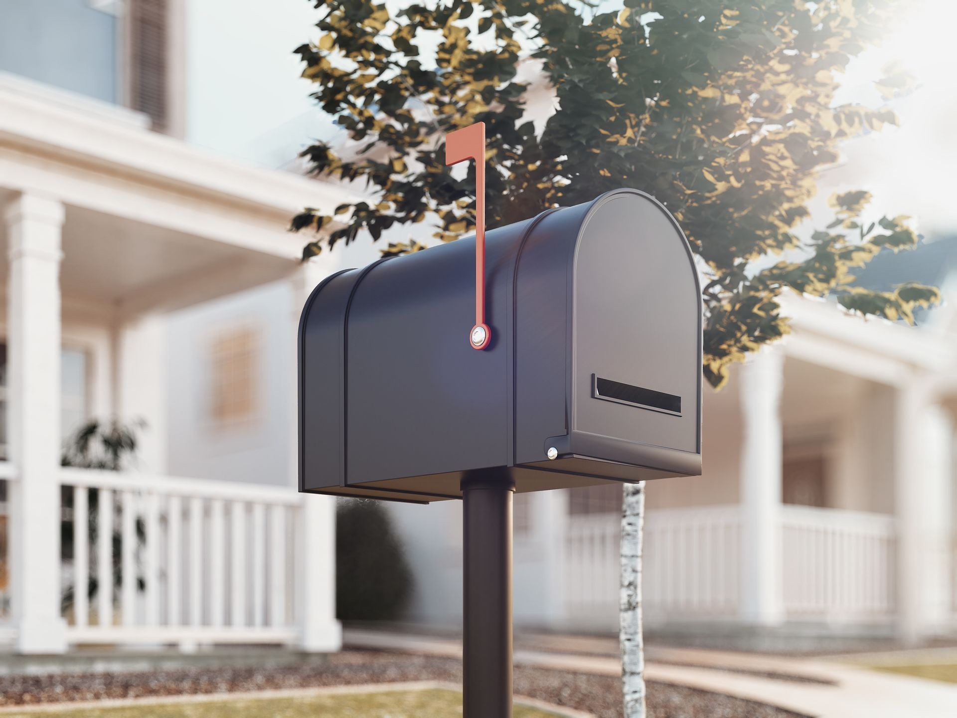 Gray mailbox on a post outside a white house with a red flag raised, in front of trees and a porch.