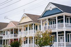Blue-gray two-story house with a manicured lawn, shrubs, and a tree-lined front yard