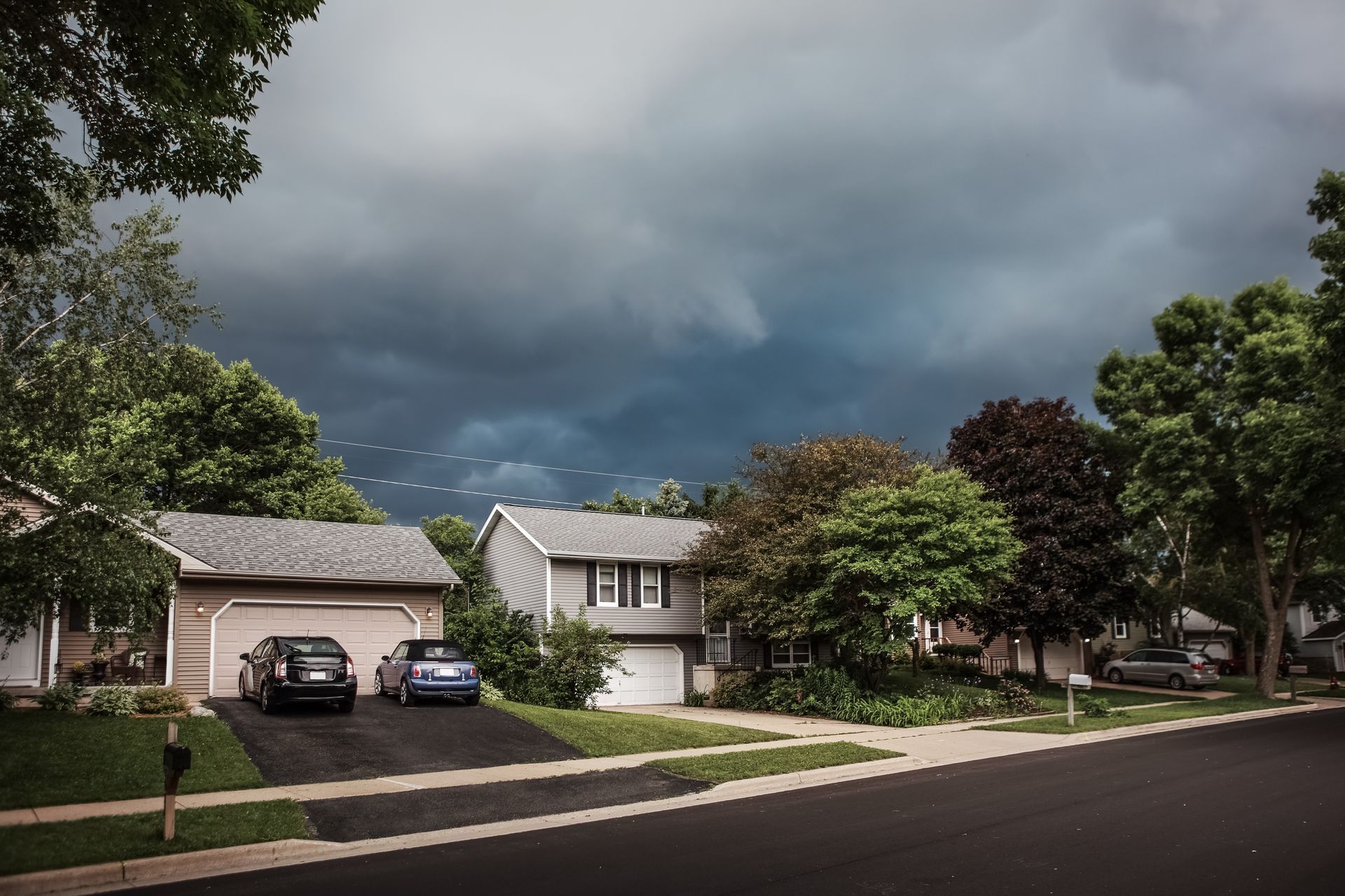Suburban street with houses, trees, parked cars, and dark storm clouds overhead
