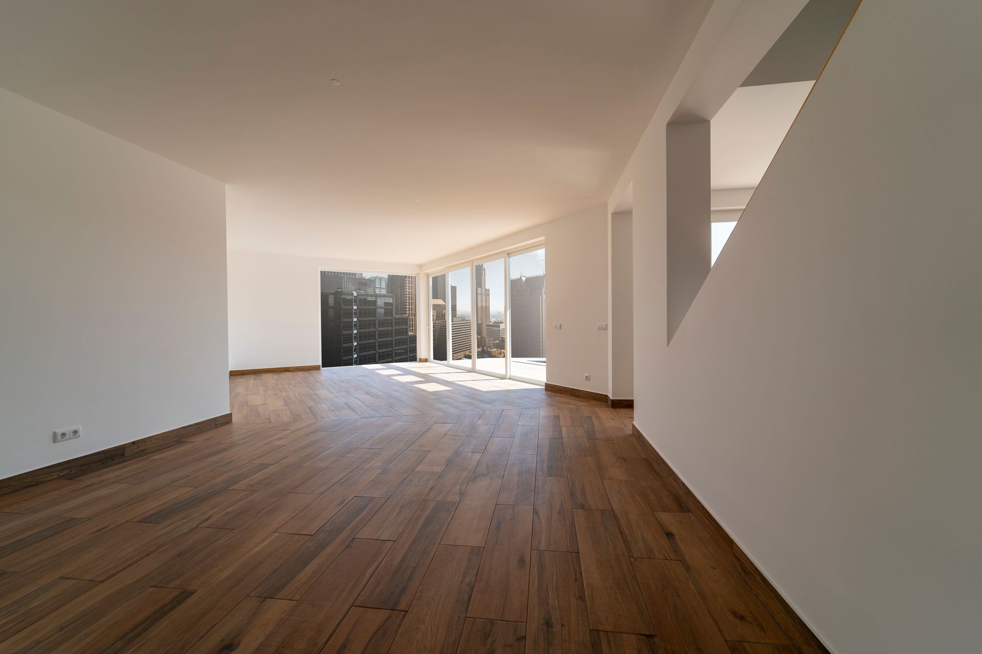 Empty modern apartment interior with wood floors, white walls, and large windows overlooking a city view