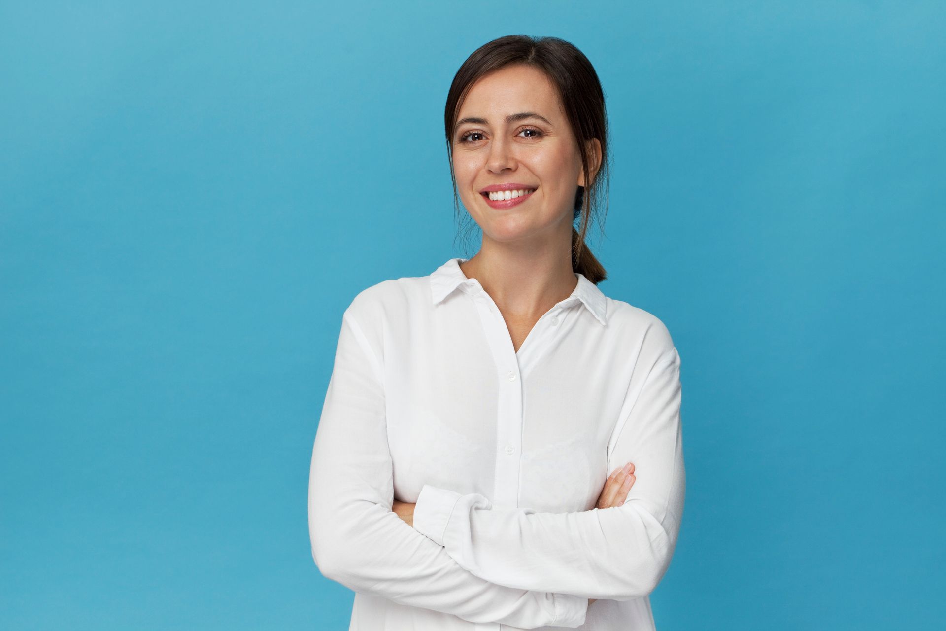 A woman in a white shirt is standing with her arms crossed and smiling.