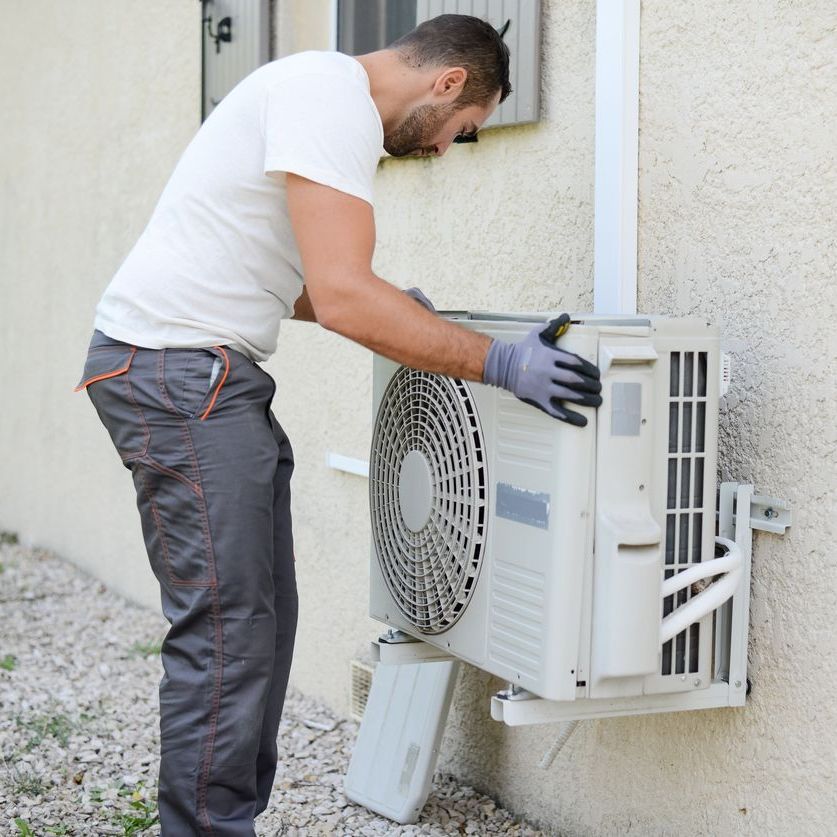 A man is installing an air conditioner on the side of a building