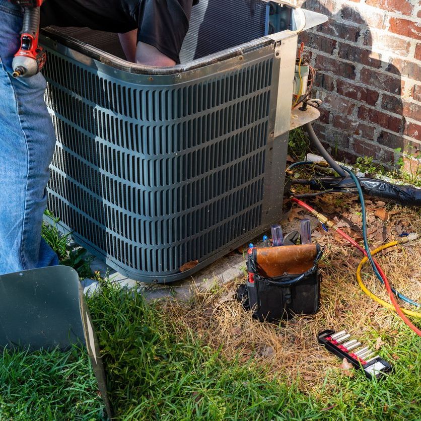 A man is working on an air conditioner outside of a brick building.