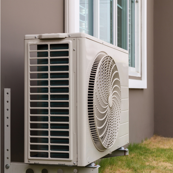 A white air conditioner is mounted on the side of a building next to a window.