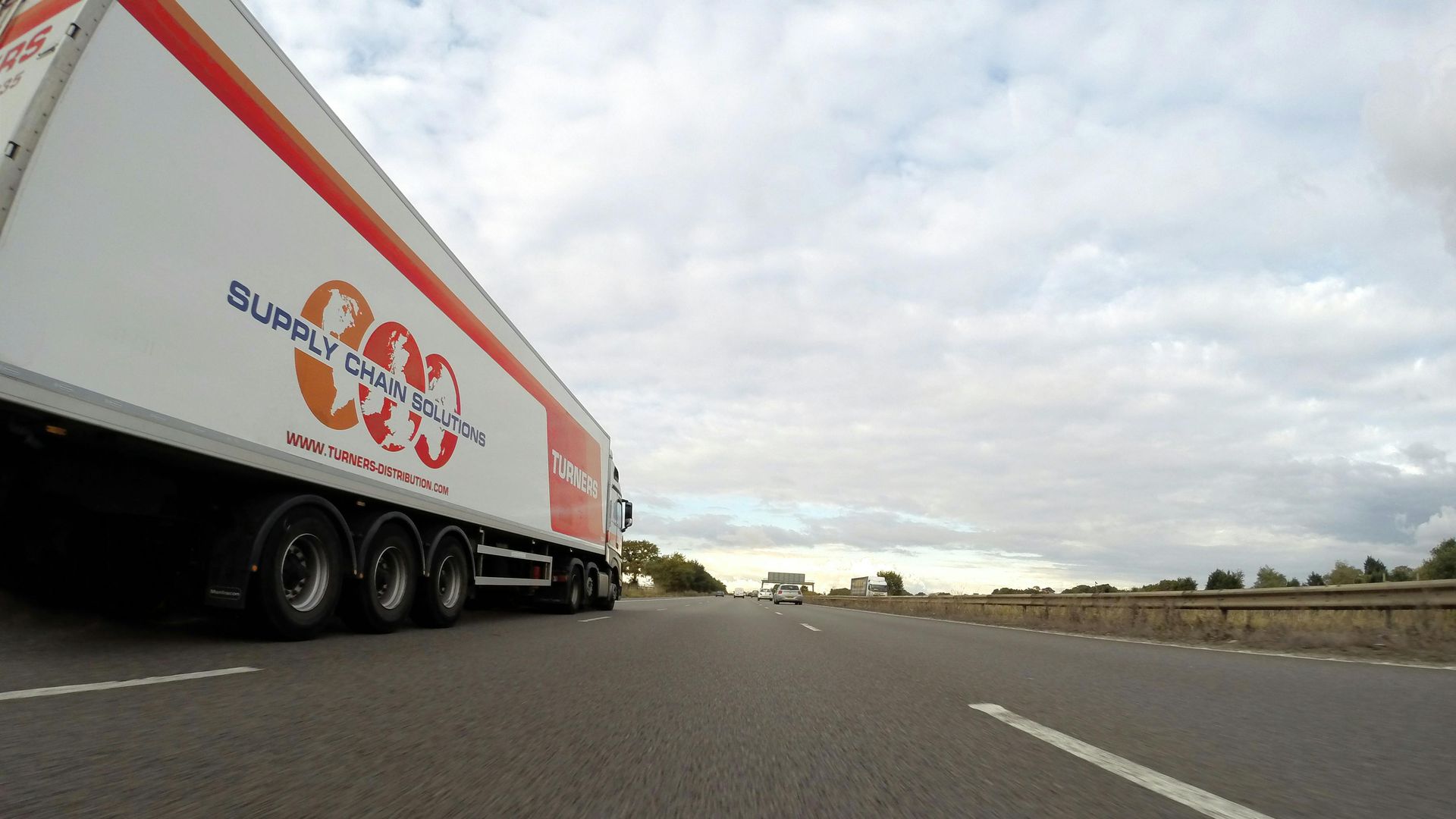 A white and red semi-trailer truck on a highway under a cloudy sky.